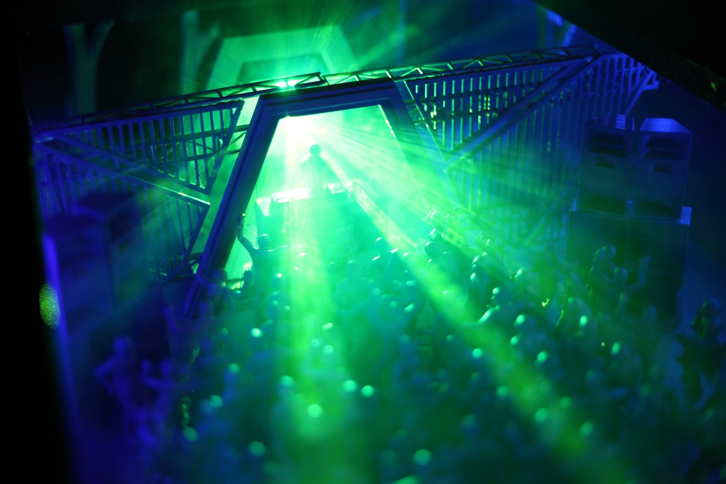 Miniature concert scene with green laser lights and a DJ stand, crowd of figures dancing.
