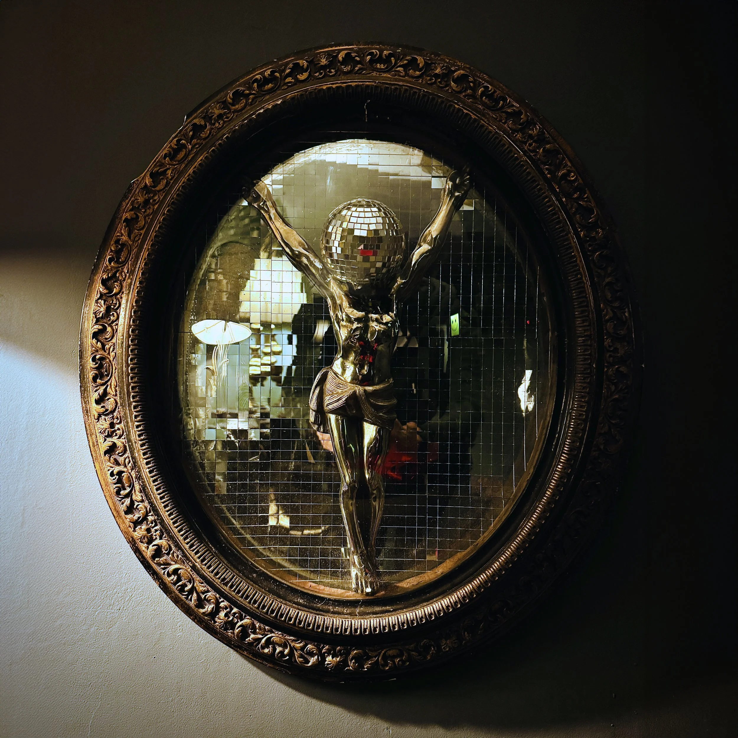 A shiny sculpture with a disco ball head inside an ornate round frame.