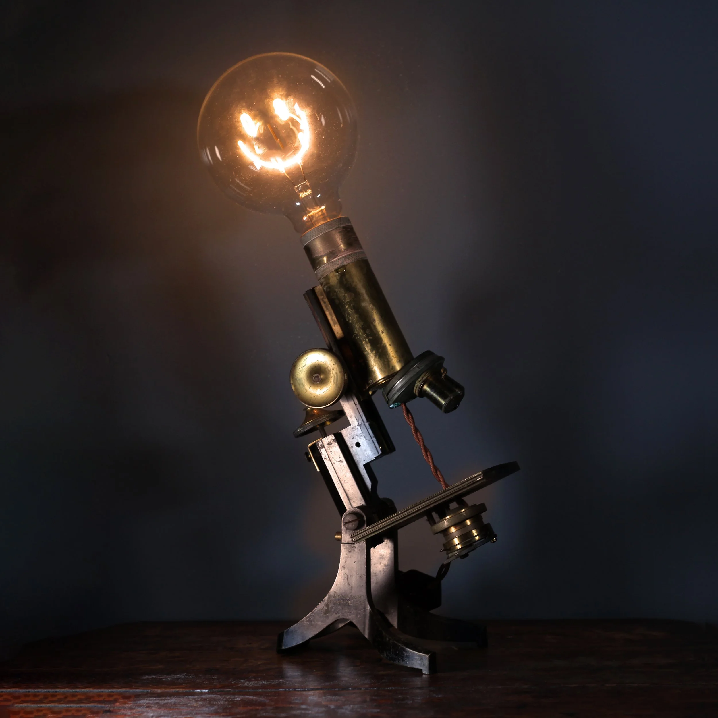 Vintage microscope with a large glowing bulb attached, placed on a wooden surface.