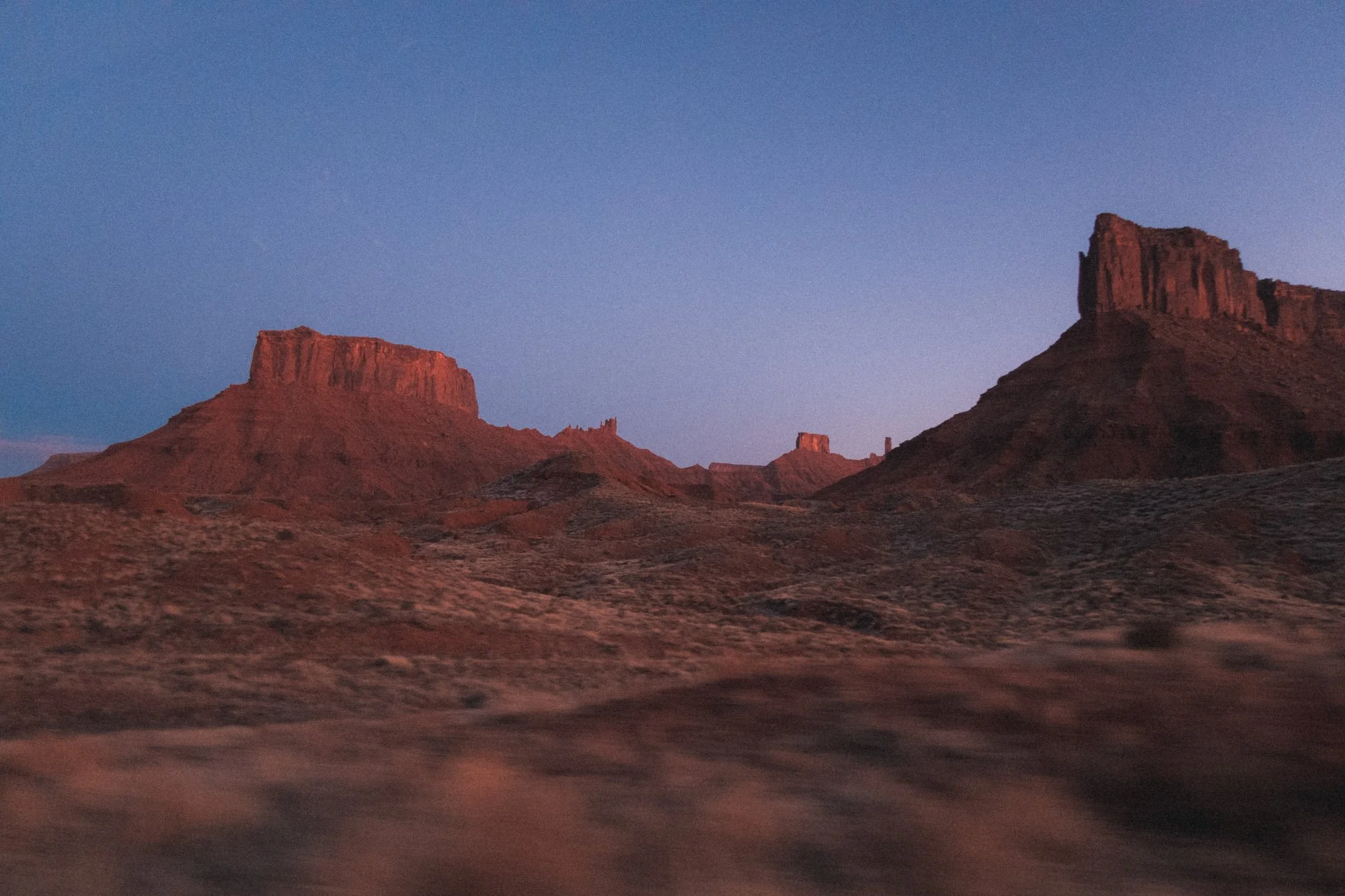 Red sandstone desert mesas and cliffs silhouetted against a blue-purple sky from a drive out of Moab