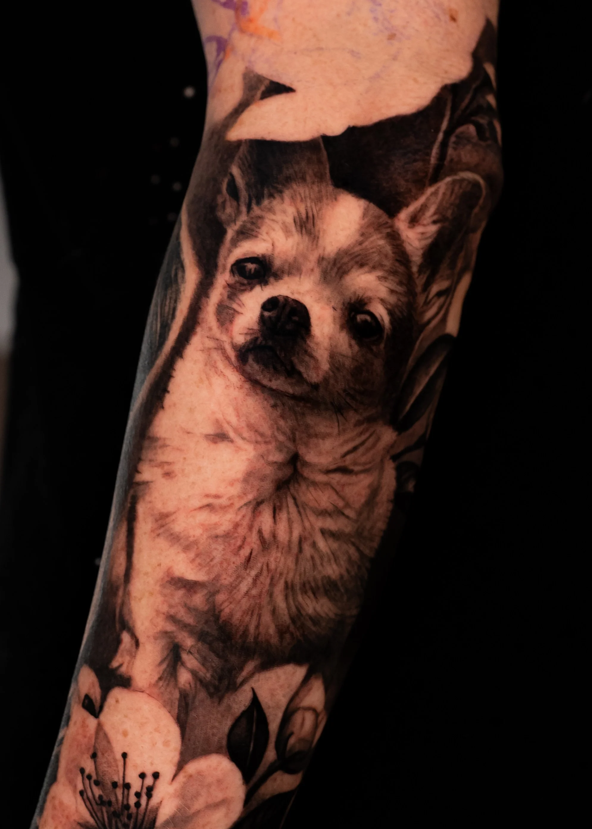 Close-up of a tattoo depicting a puppy and pink flowers on someone's arm.