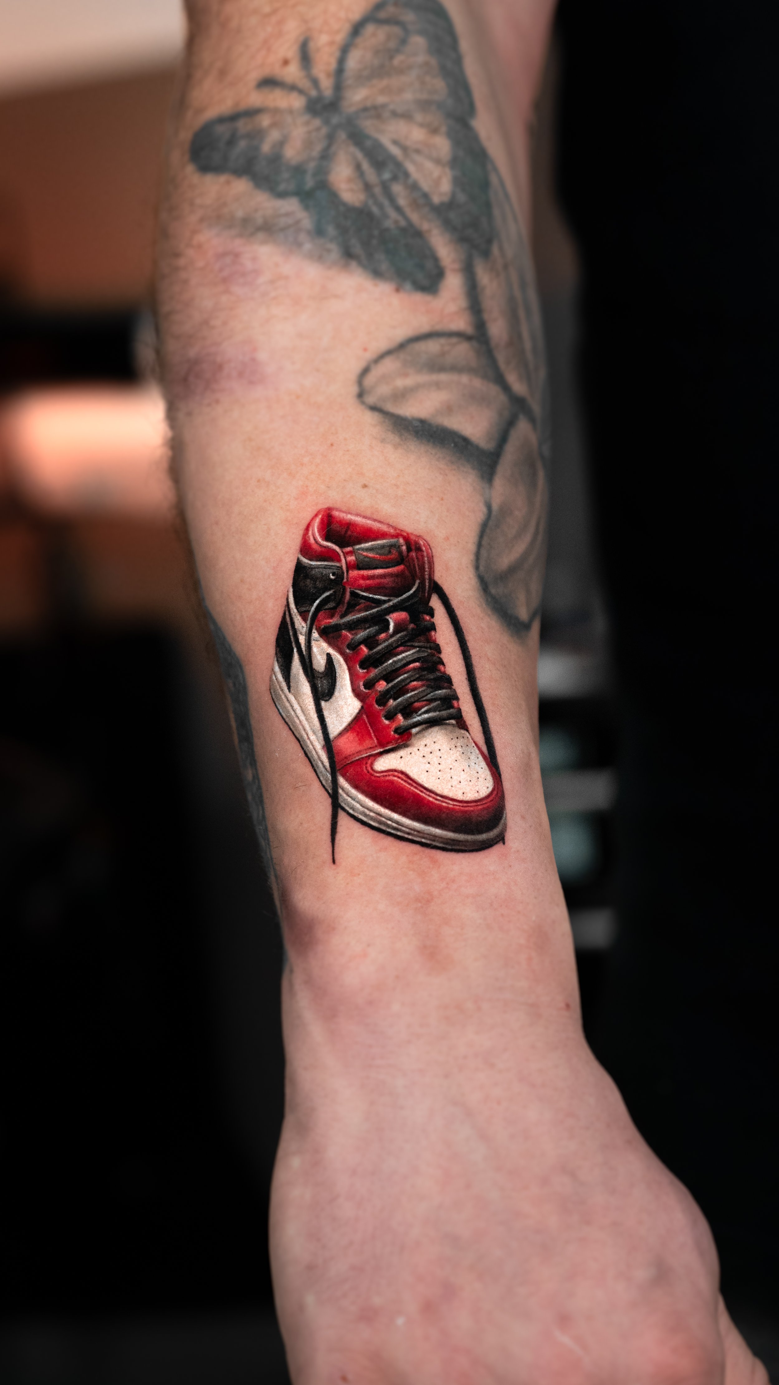 Tattoo of a red and white sneaker on a person's lower leg below the knee.