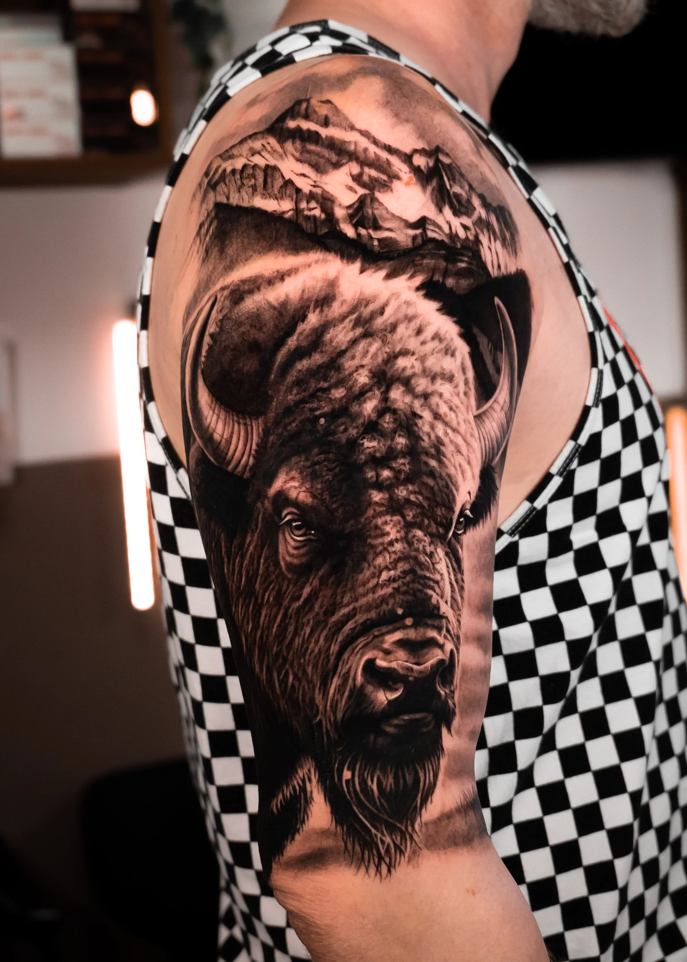 Black and gray detailed tattoo of a bear's face with trees and mountains on a person's upper arm.