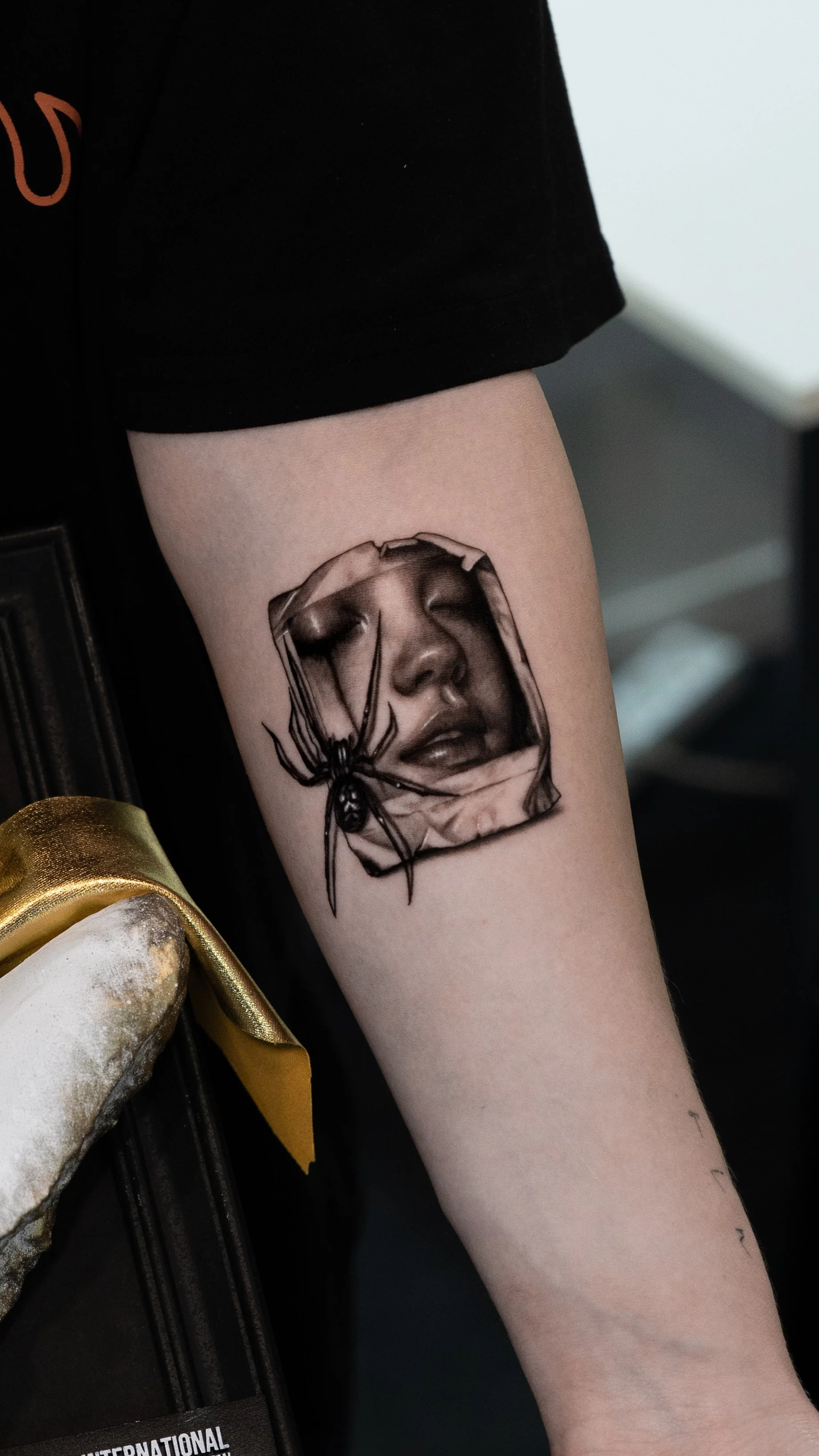 Tattoo of a woman's face with closed eyes and lips, surrounded by a spider on the arm.