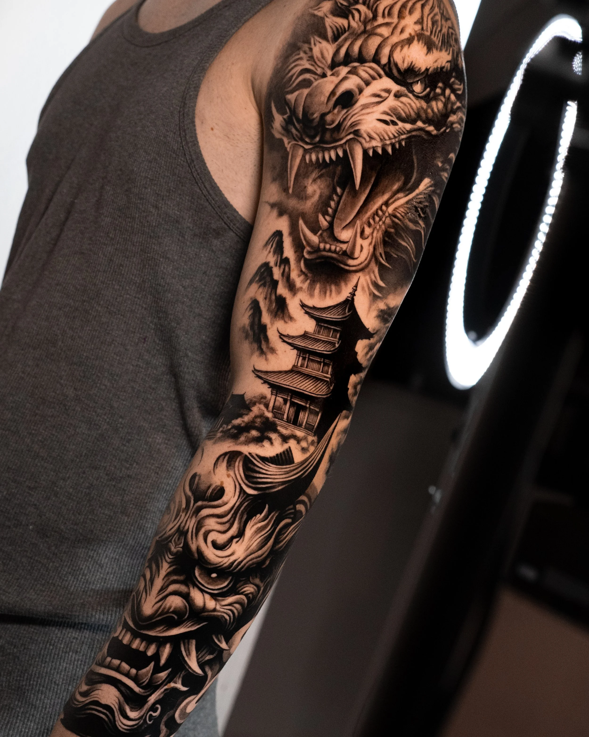 Close-up of a person's arm with a detailed black and gray tattoo of a fierce tiger's face and a traditional pagoda-style building.