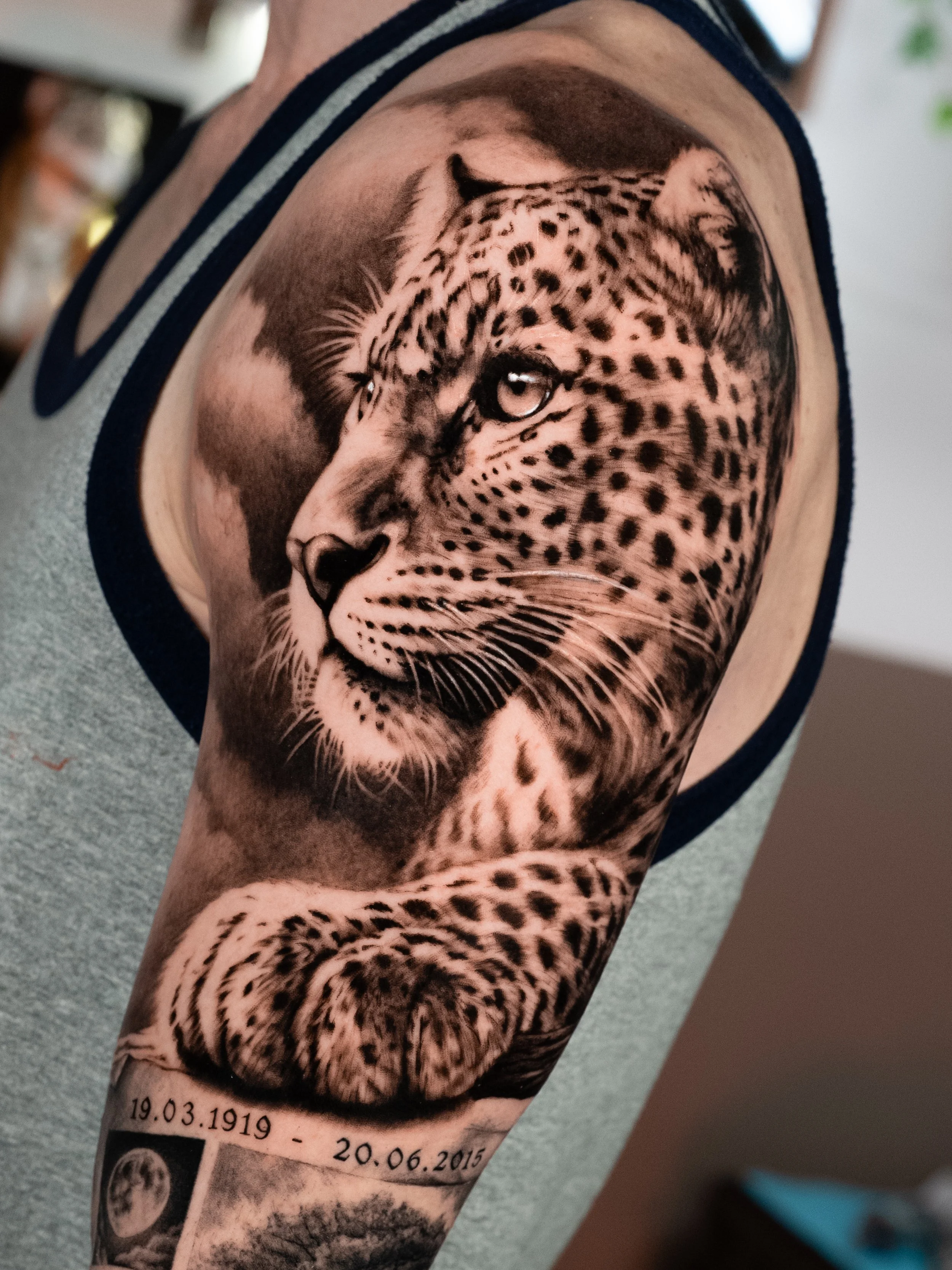 Tattoo of a realistic leopard's face on a person's arm, with dates and small photographs below.