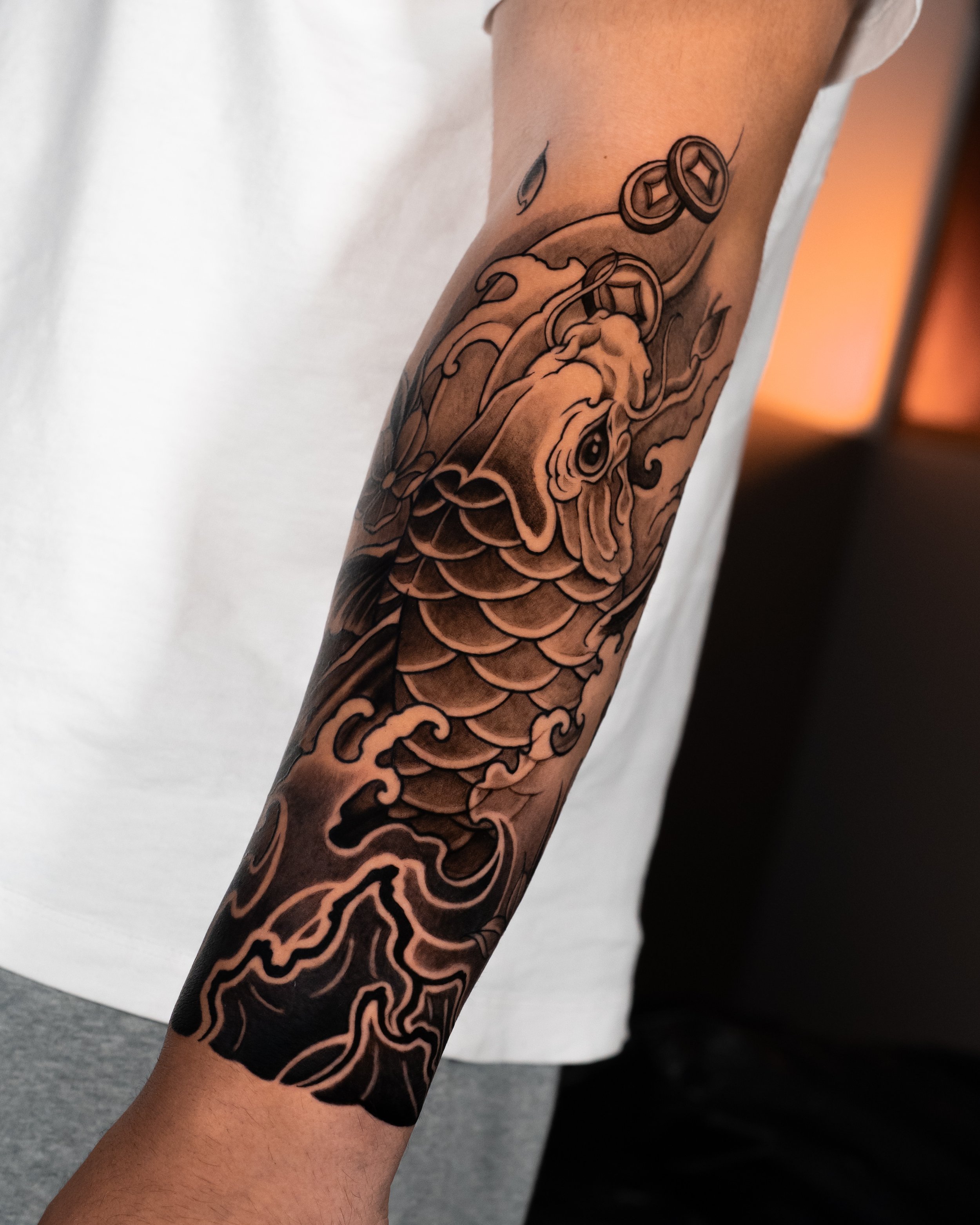 Close-up of a person's arm with a black and gray tattoo of a dragon and coins.