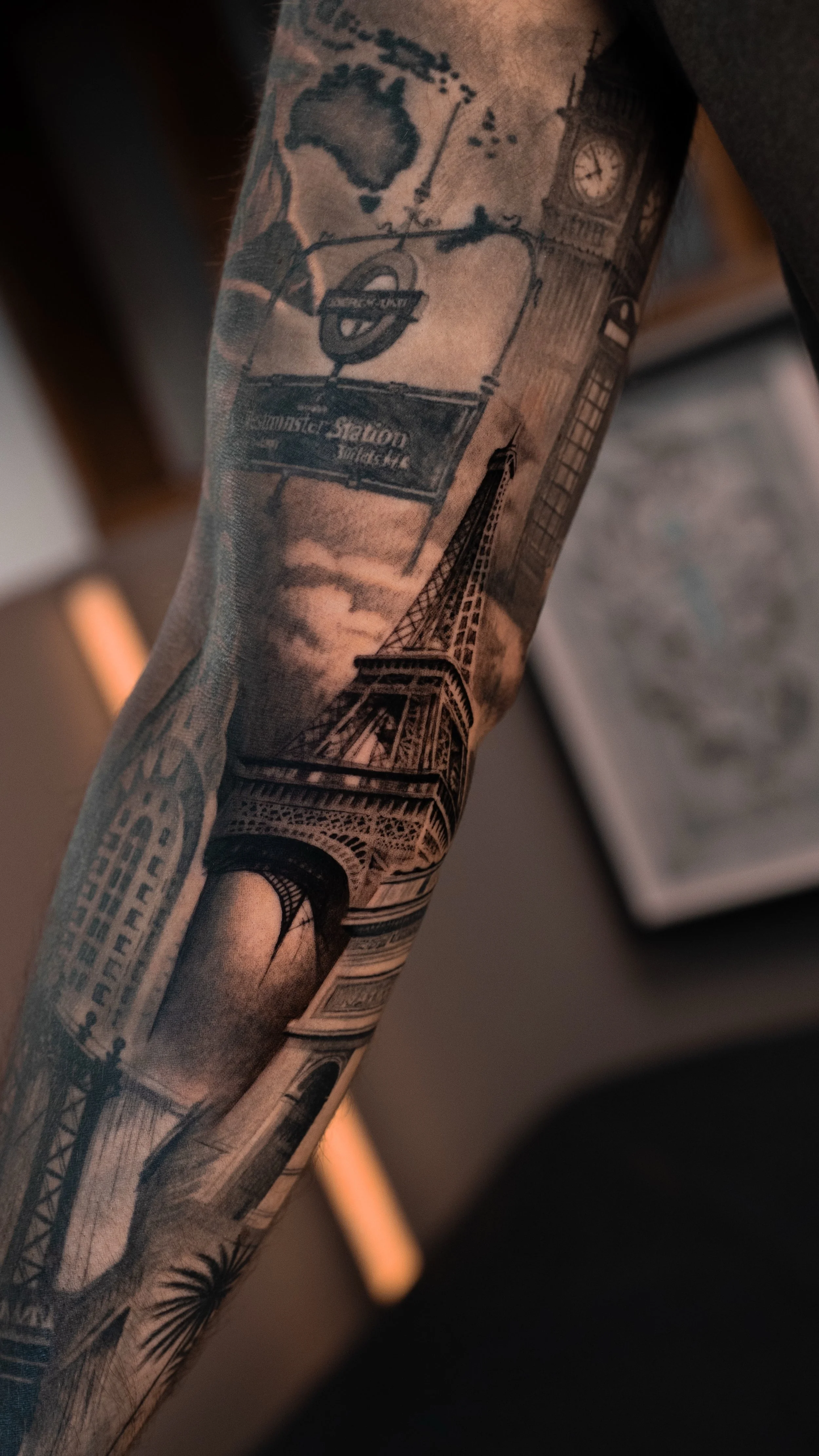 Black and gray tattoo sleeve featuring Big Ben, the Eiffel Tower, a London Underground sign, and a world map.