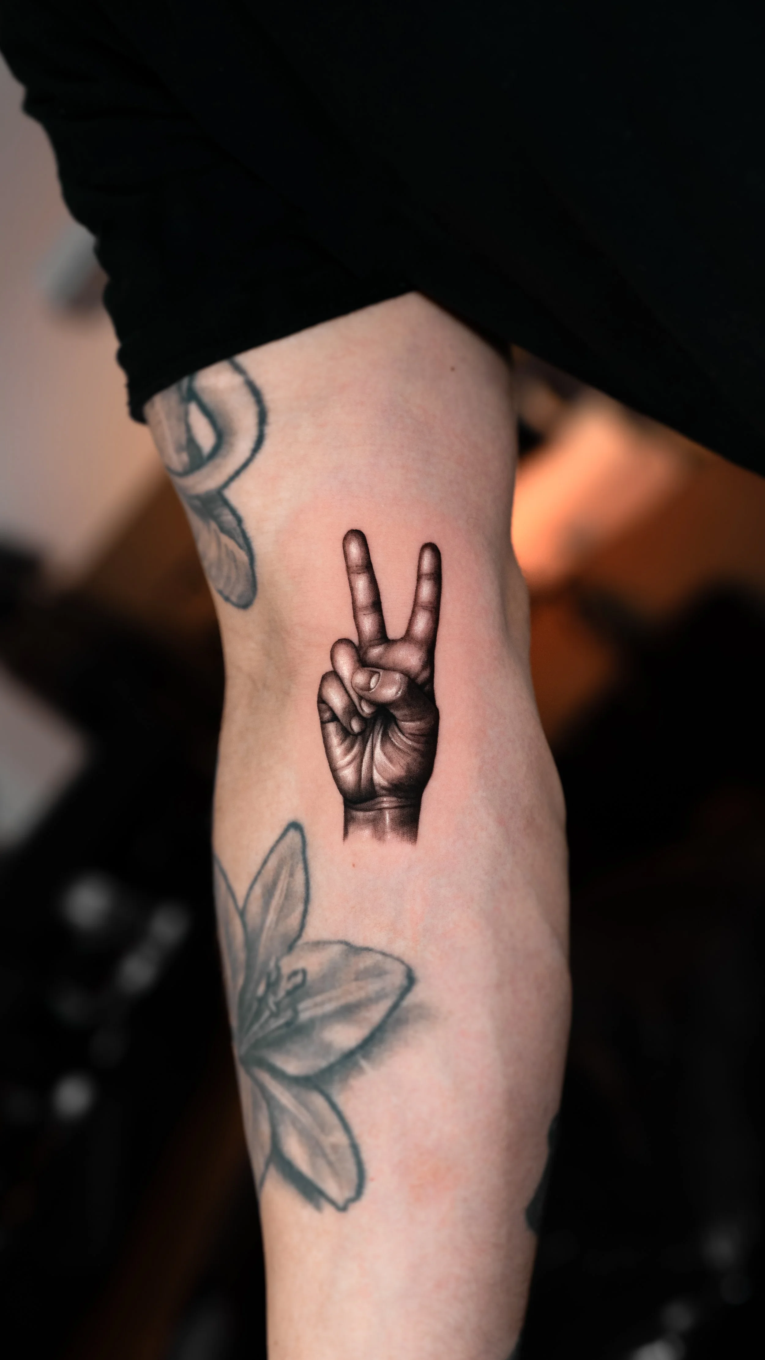 Tattoo of a realistic hand showing a peace sign on a person's forearm.