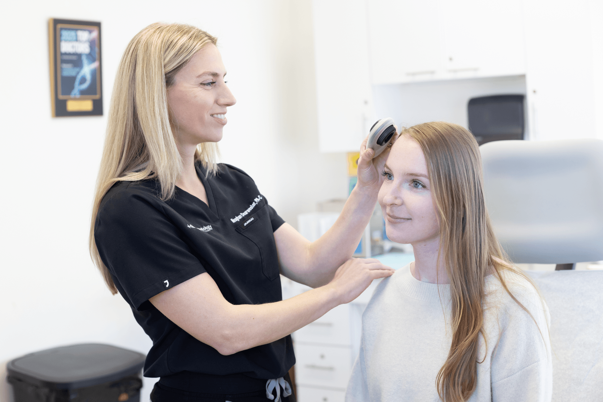 Healthcare professional examining a young woman's head with an otoscope in a clinic setting.