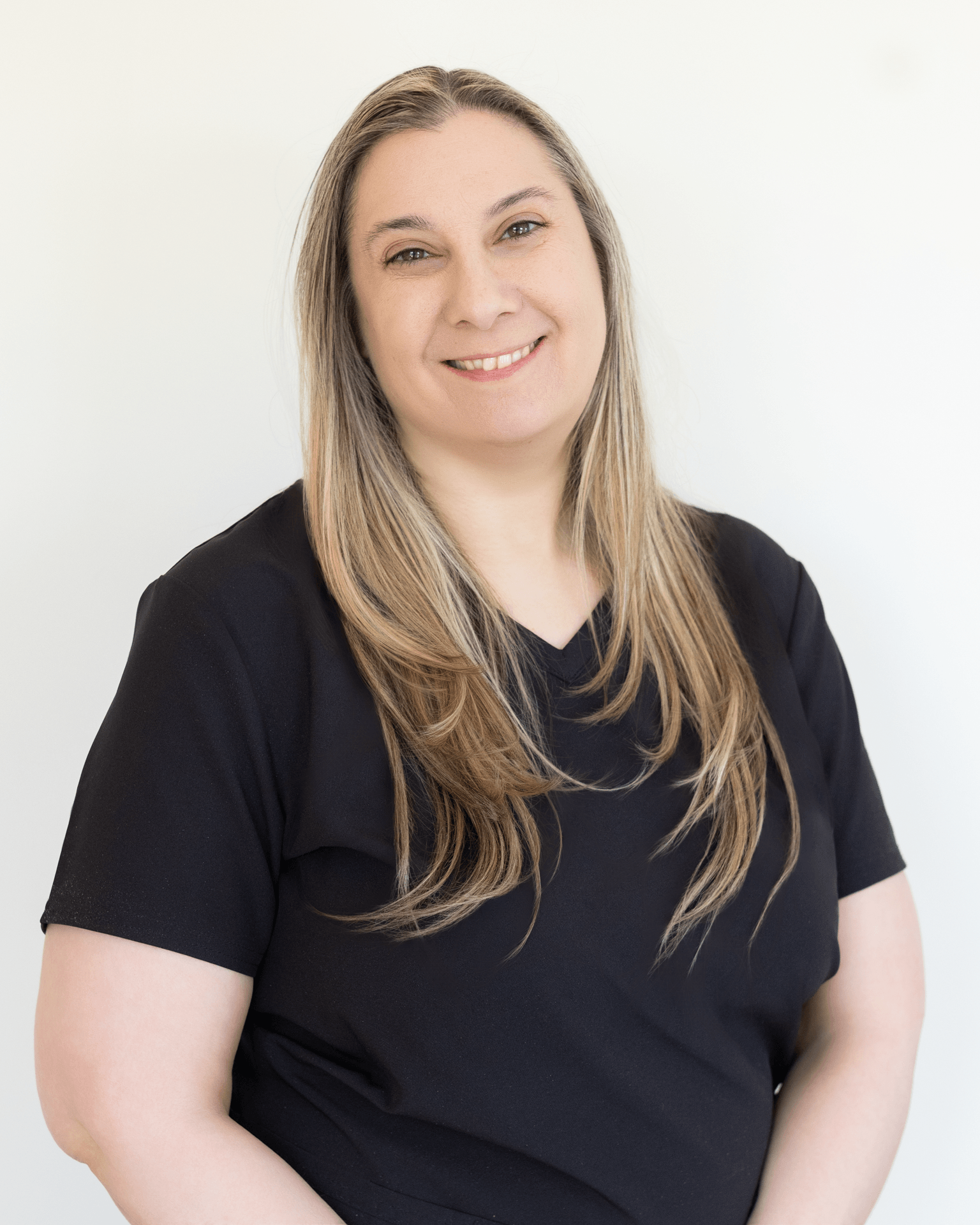 A woman with long light brown hair, wearing a black t-shirt, smiling against a plain white background.