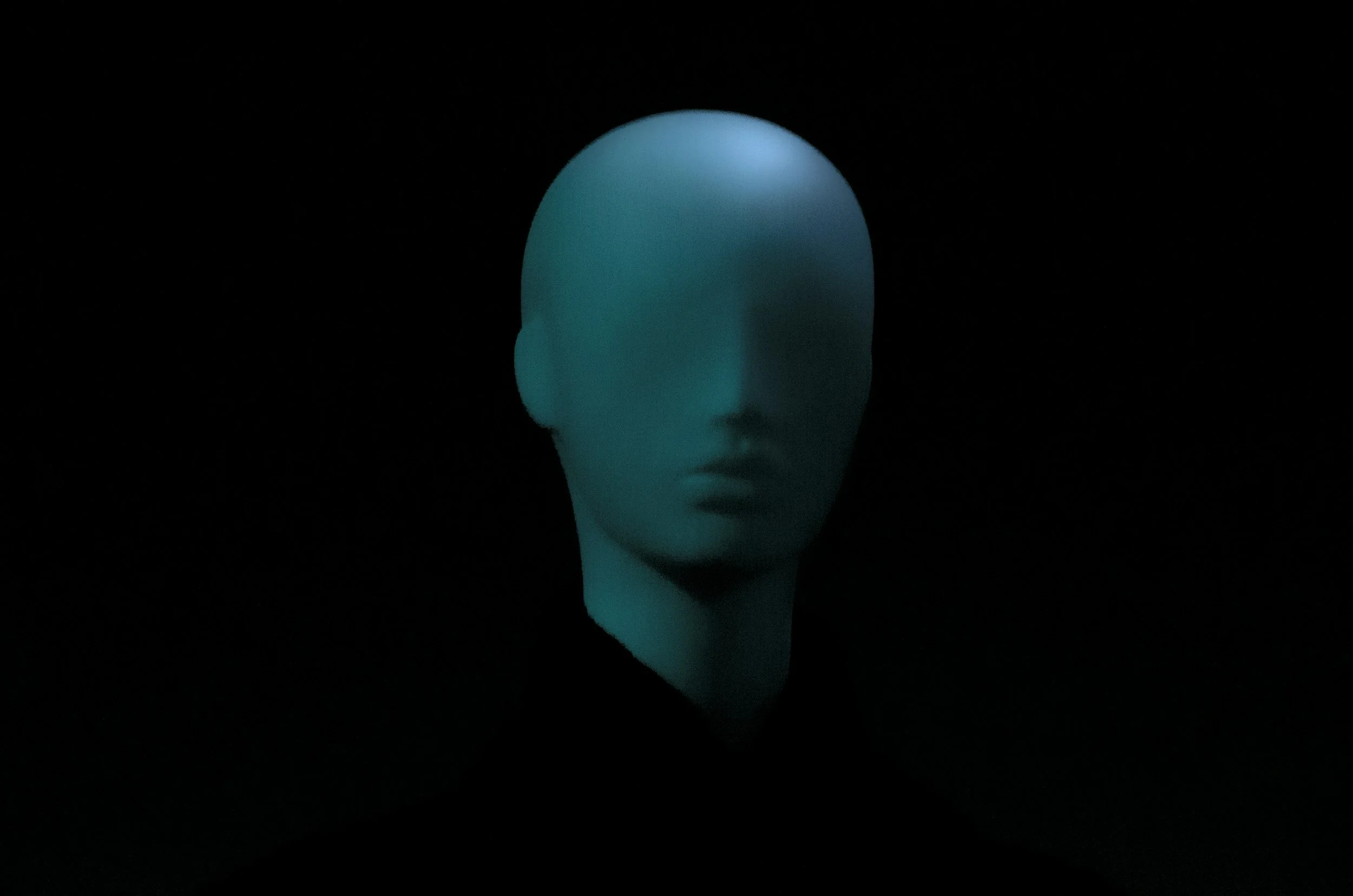 A mannequin head with featureless face, illuminated with soft blue light against a black background.
