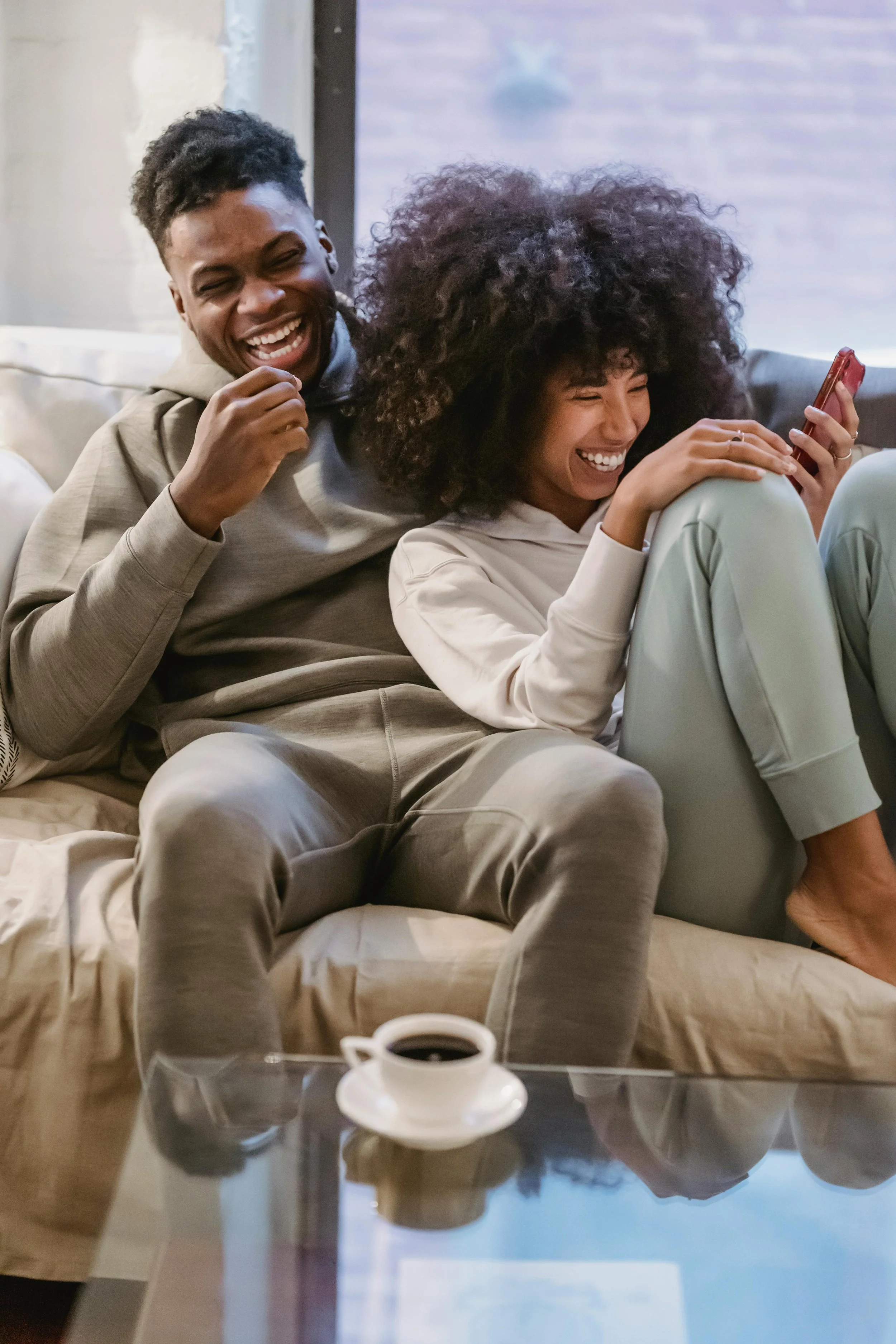 two people laughing on the couch with their phones