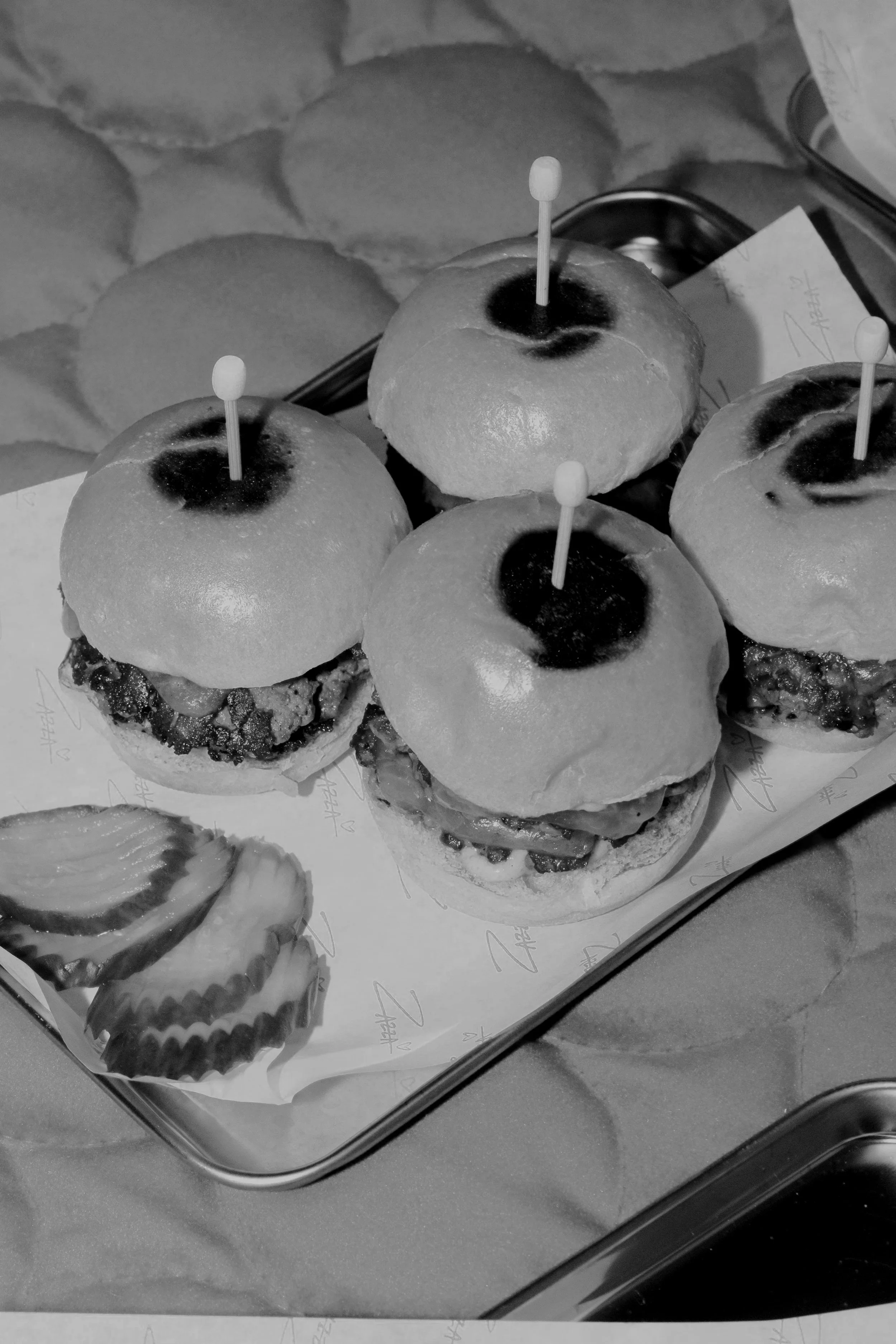 Mini sliders with buns, meat, and toppings served on a wooden tray with toothpicks.