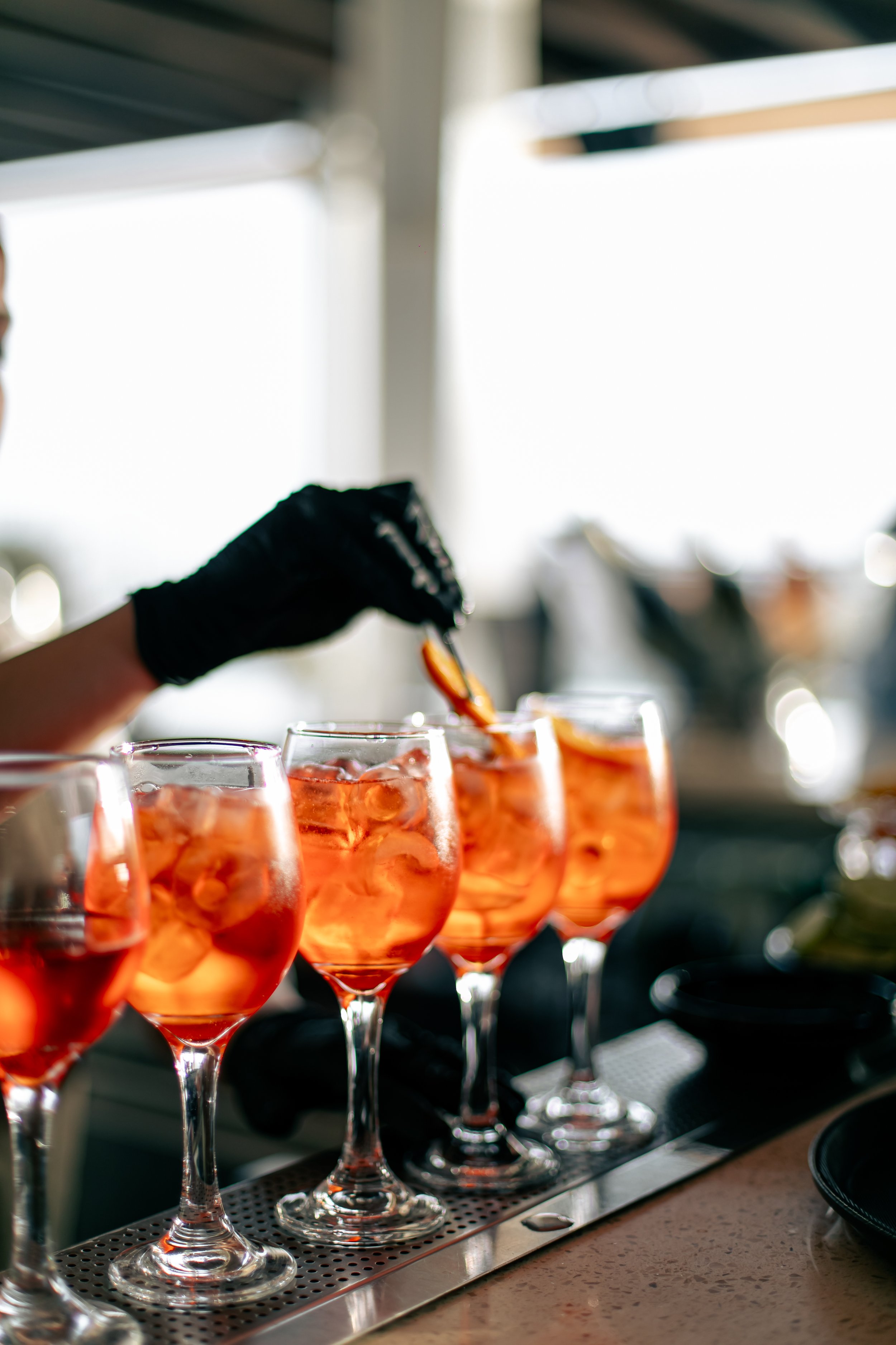 A person wearing a black glove is placing fruit slices into wine glasses filled with orange-colored beverages on a bar counter.