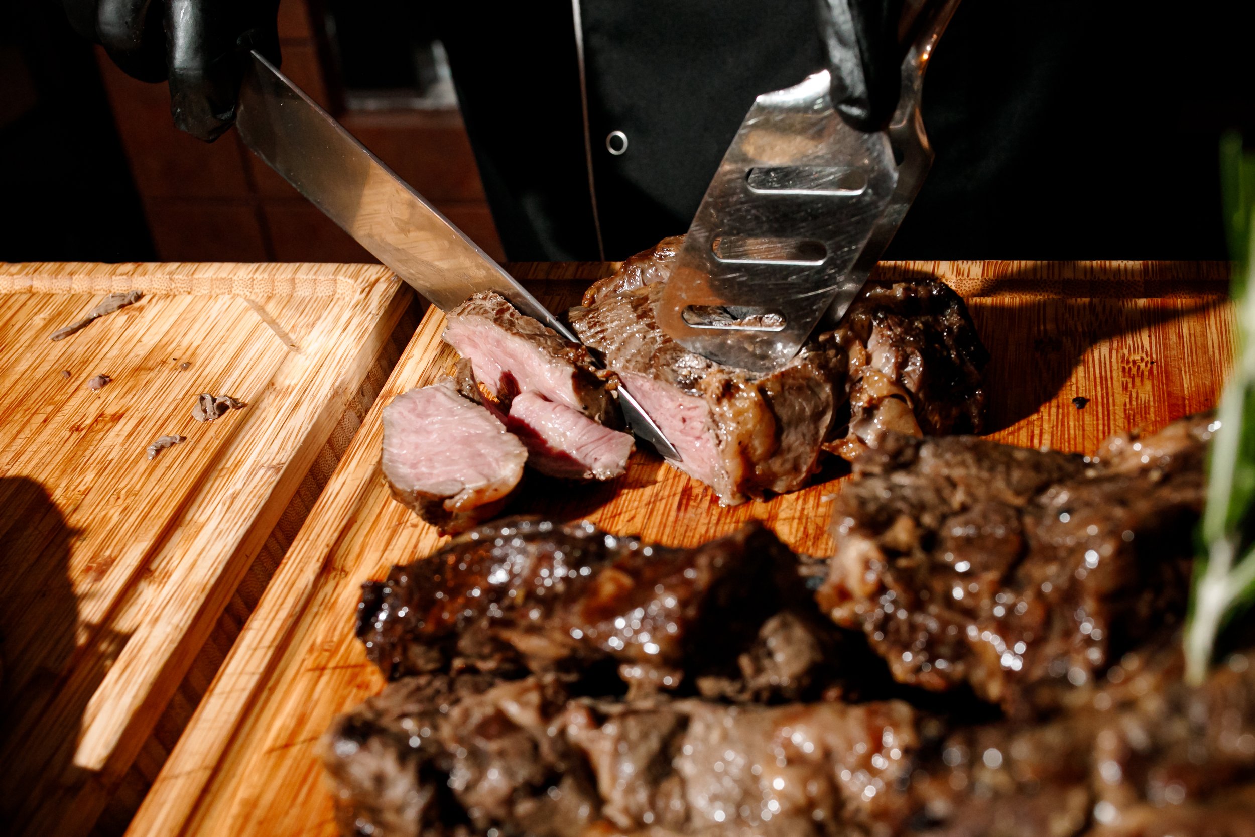 Person slicing medium-rare cooked steak on a wooden cutting board.