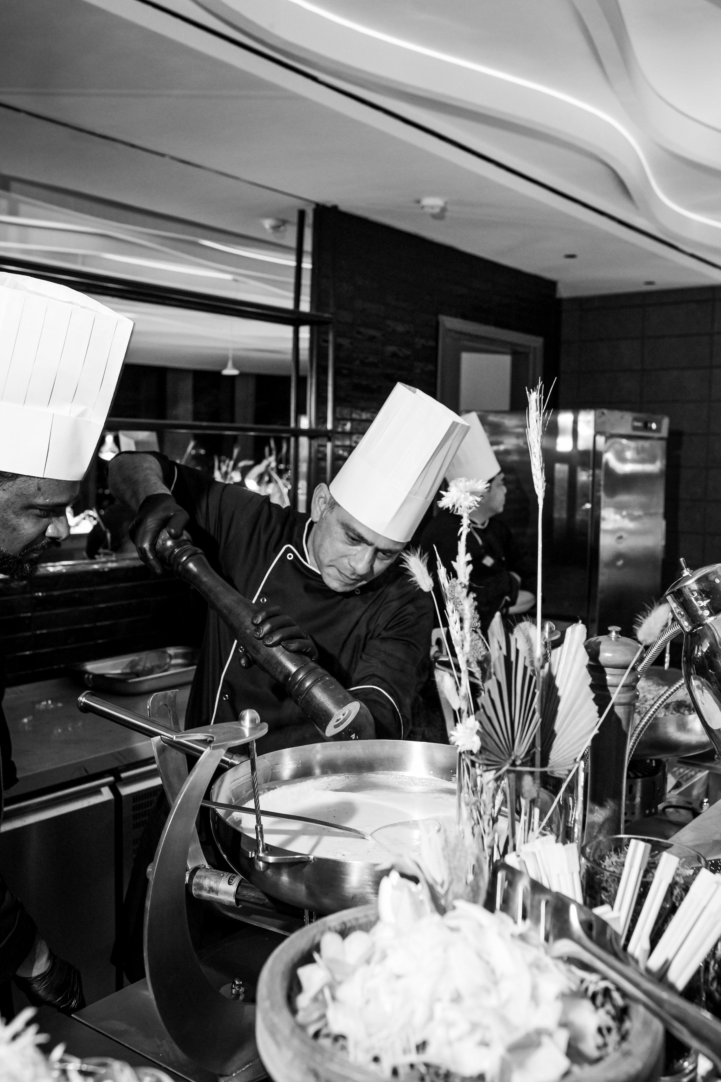 Black and white photo of chefs in white hats preparing food in a restaurant kitchen.