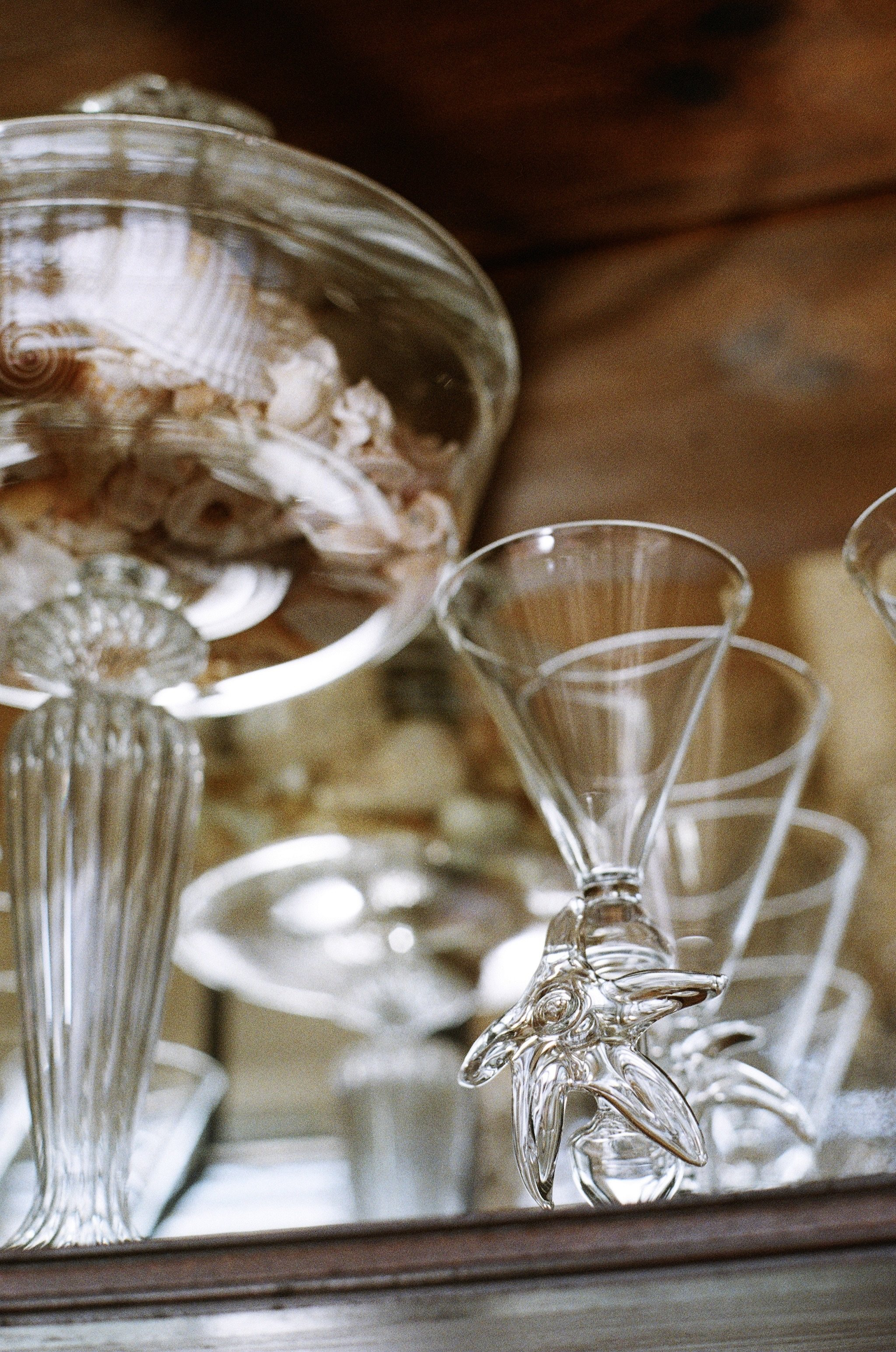 A collection of clear glass dessert cups, including martini glasses, displayed on a mirrored surface with a wooden background.