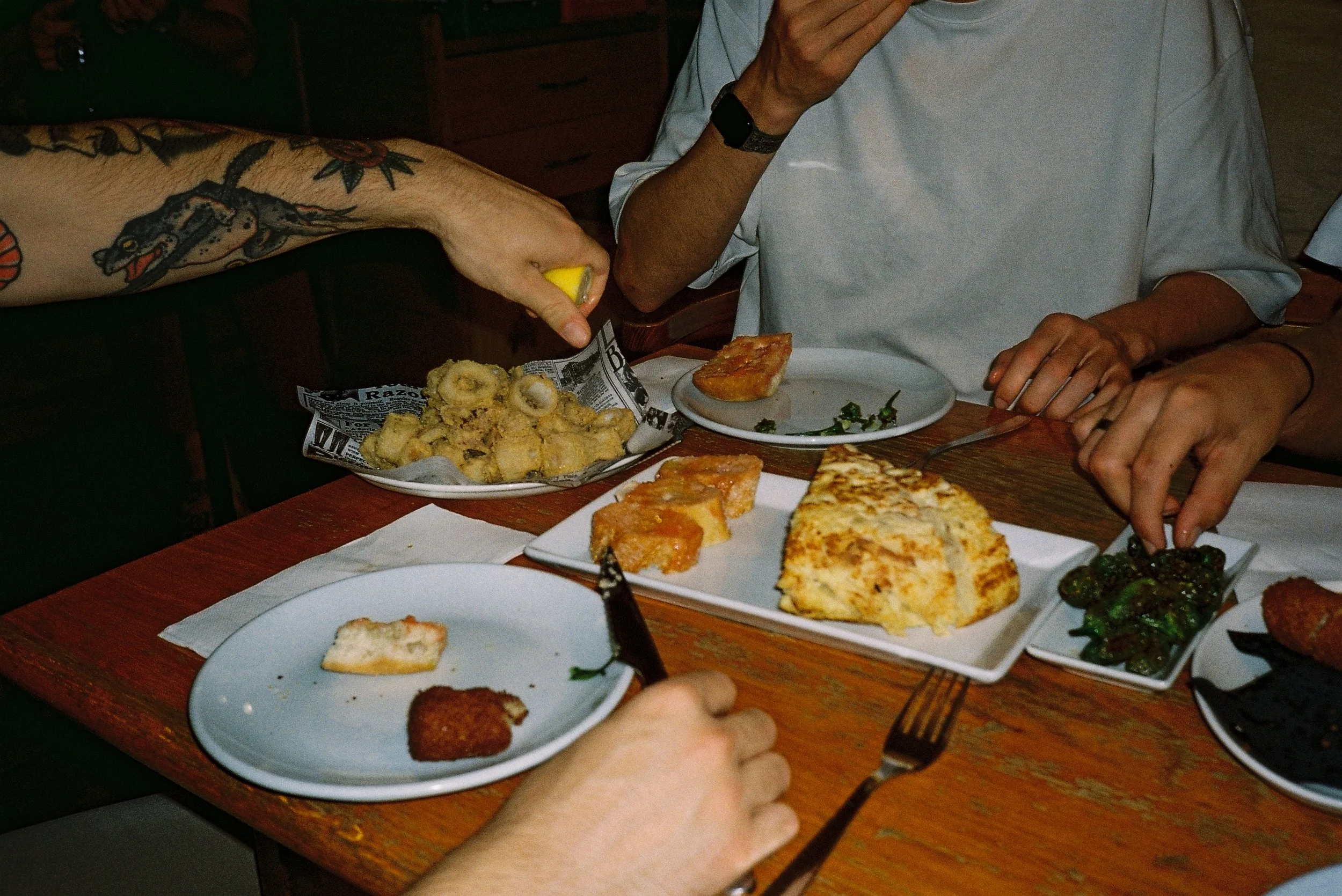 People sharing a meal at a restaurant, with plates of fried food, cake, and vegetables on the wooden table.