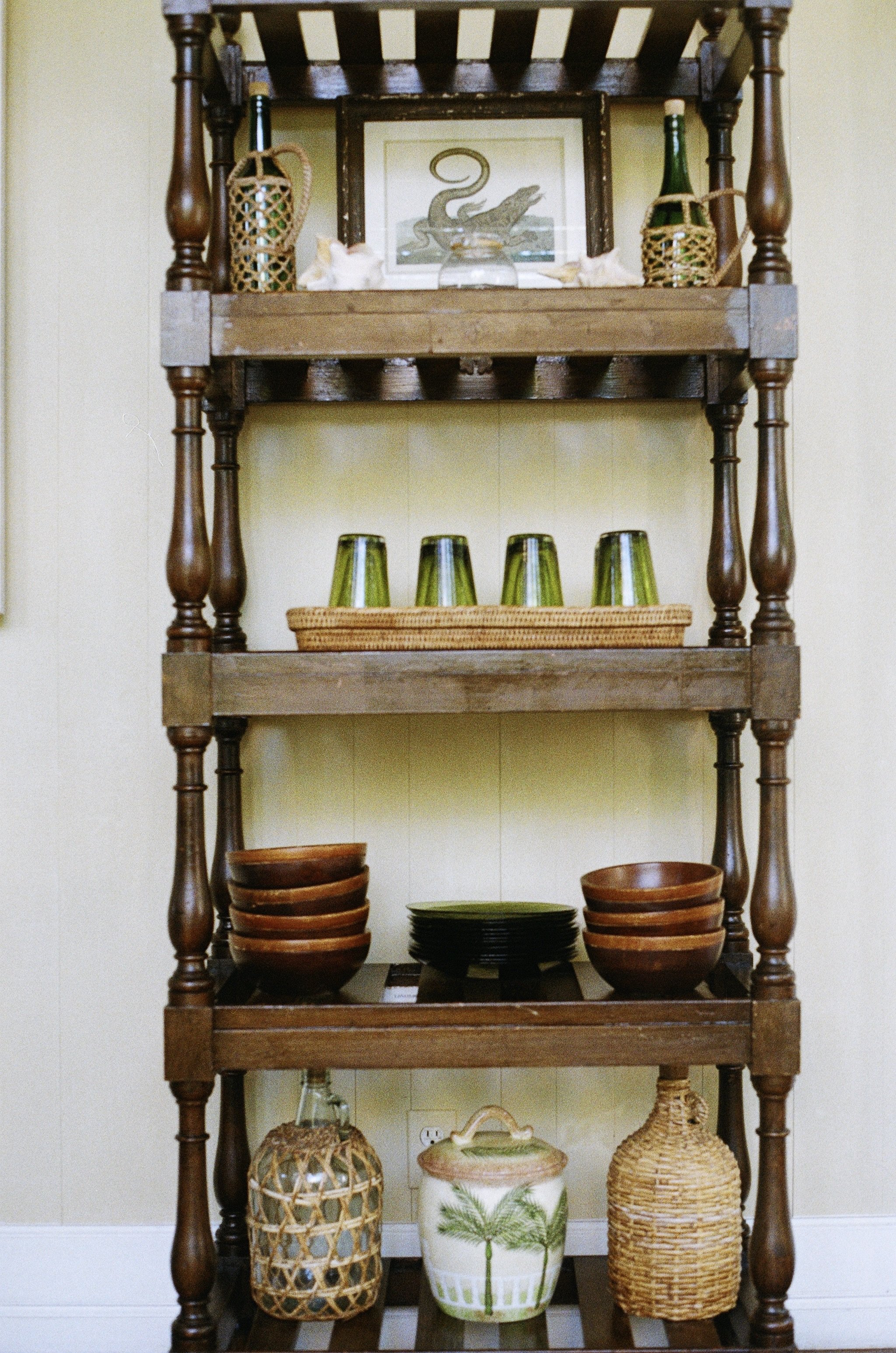 A wooden shelving unit displaying decorative items, including framed artwork, glassware, bowls, plates, and woven baskets.