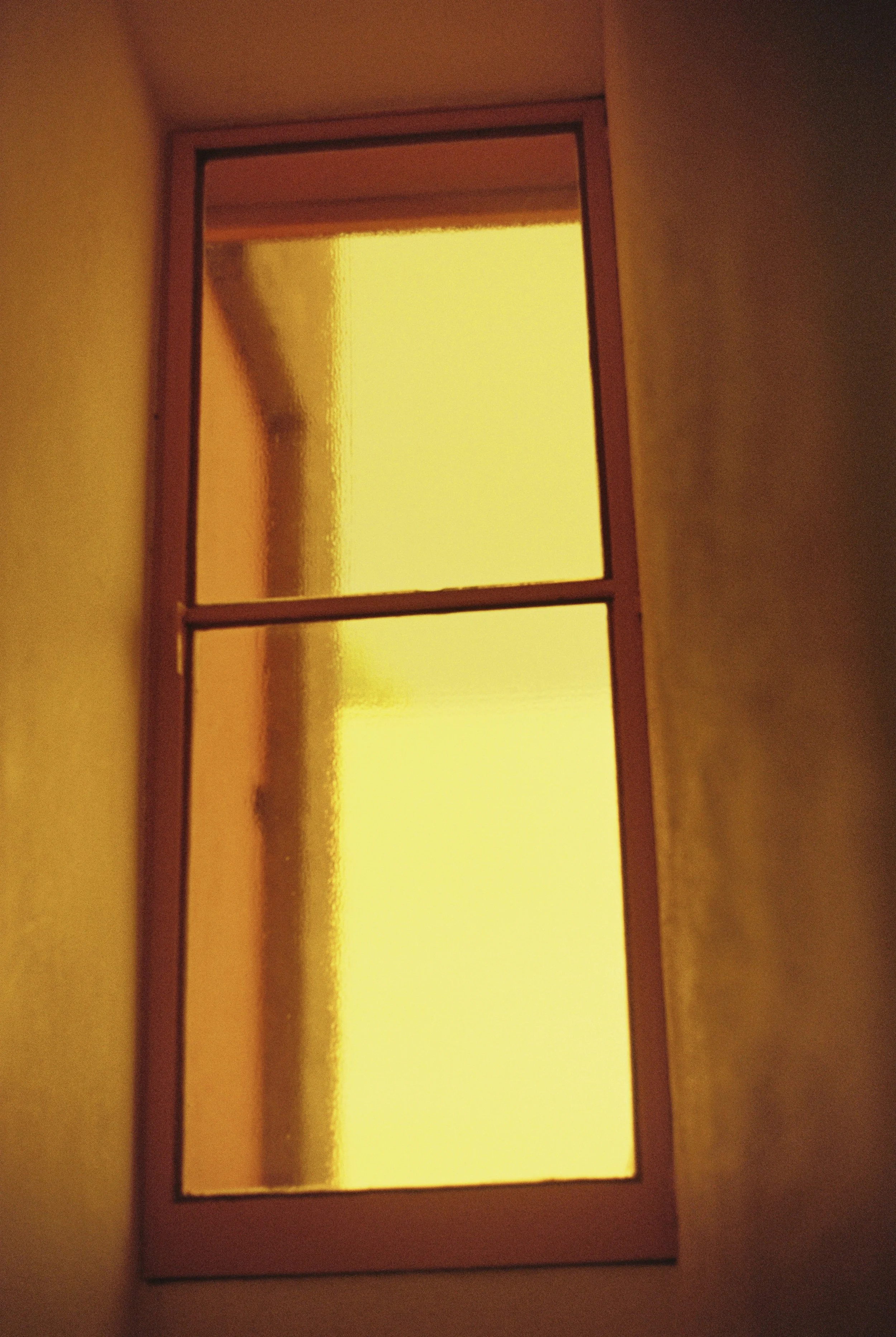 A yellow-tinted window with a small horizontal divider in the middle, framed by walls painted in a warm color.