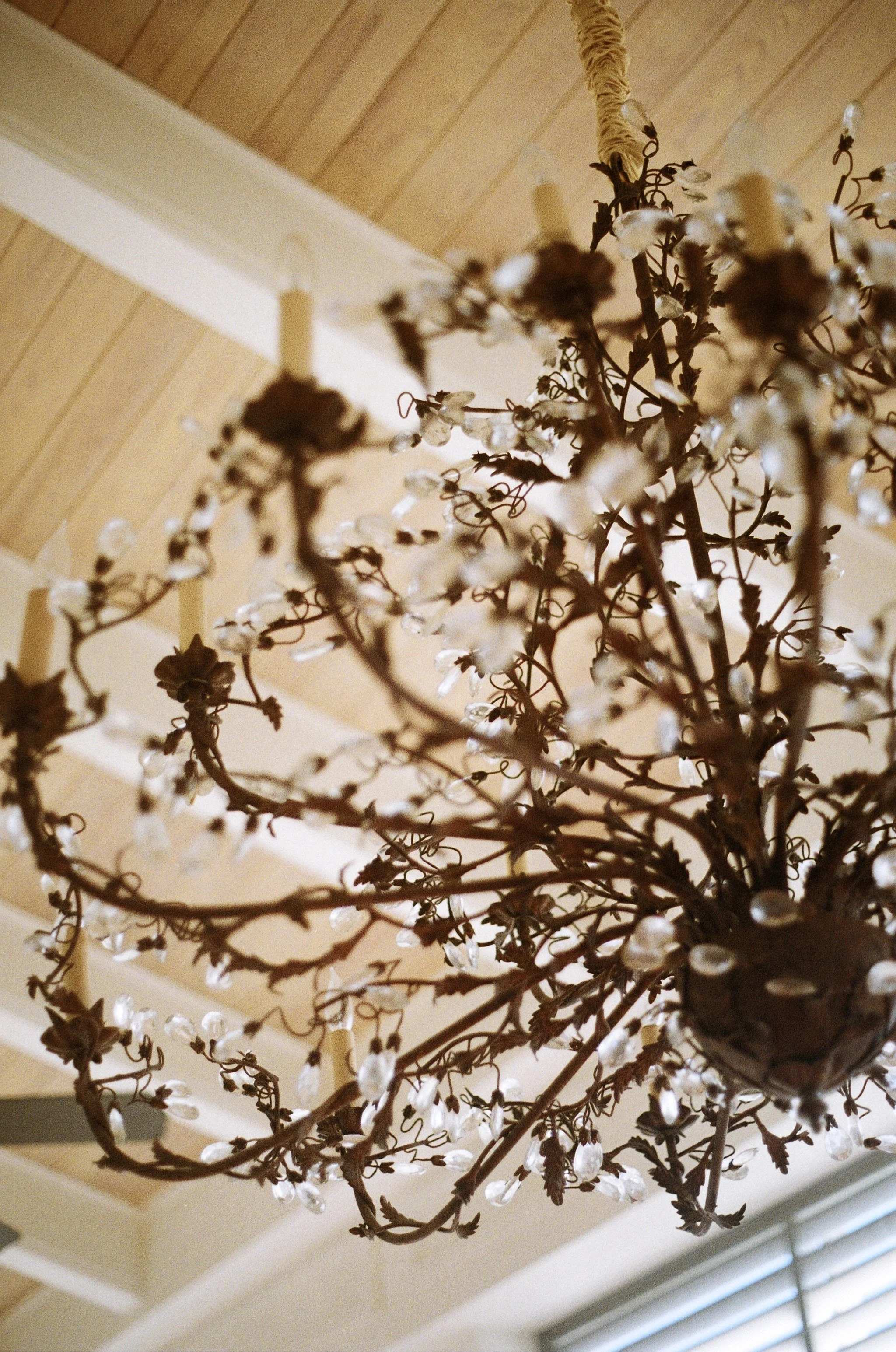 Close-up of a decorative chandelier with crystal droplets hanging from metal arms, mounted on a wooden ceiling.