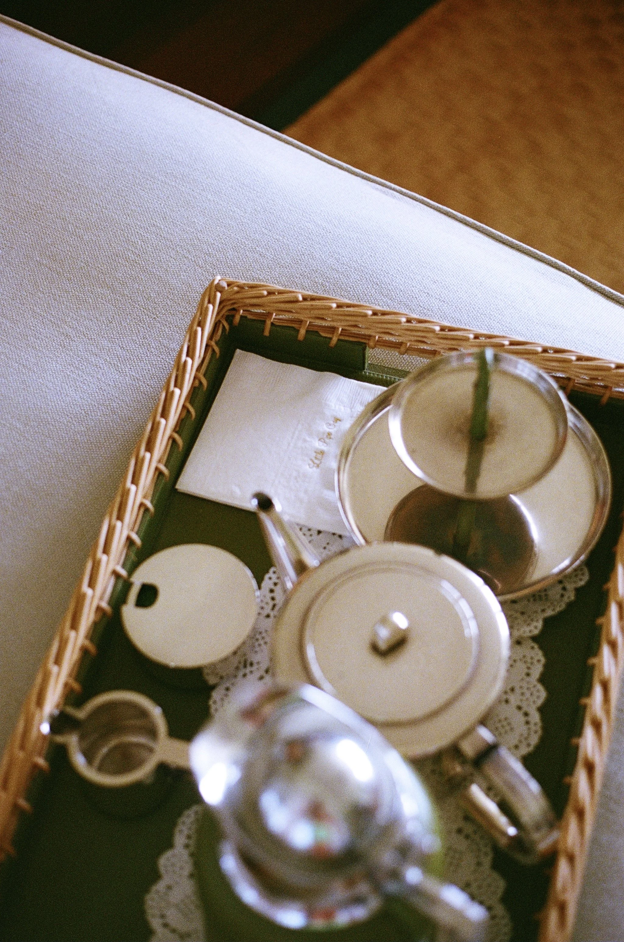 A tea set on a tray, including a teapot, sugar bowl, and creamer, placed on a doily on a table.