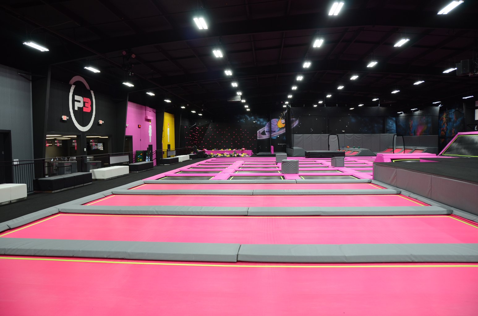 Indoor trampoline park with pink and gray trampoline beds and space-themed wall murals.