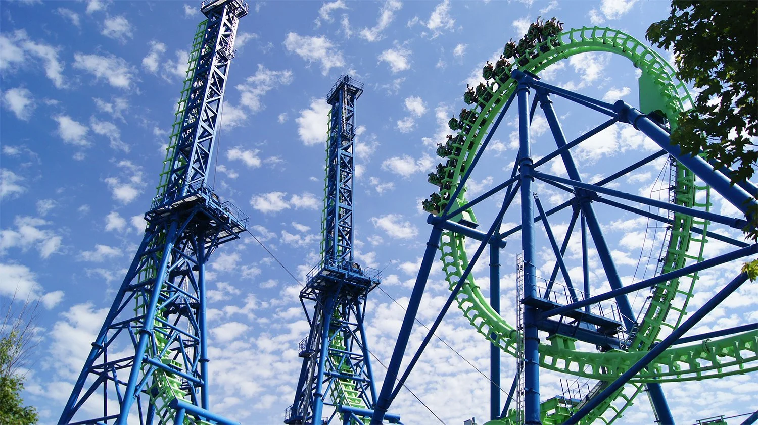 Colorful amusement park roller coaster with blue and green tracks under a partly cloudy sky.
