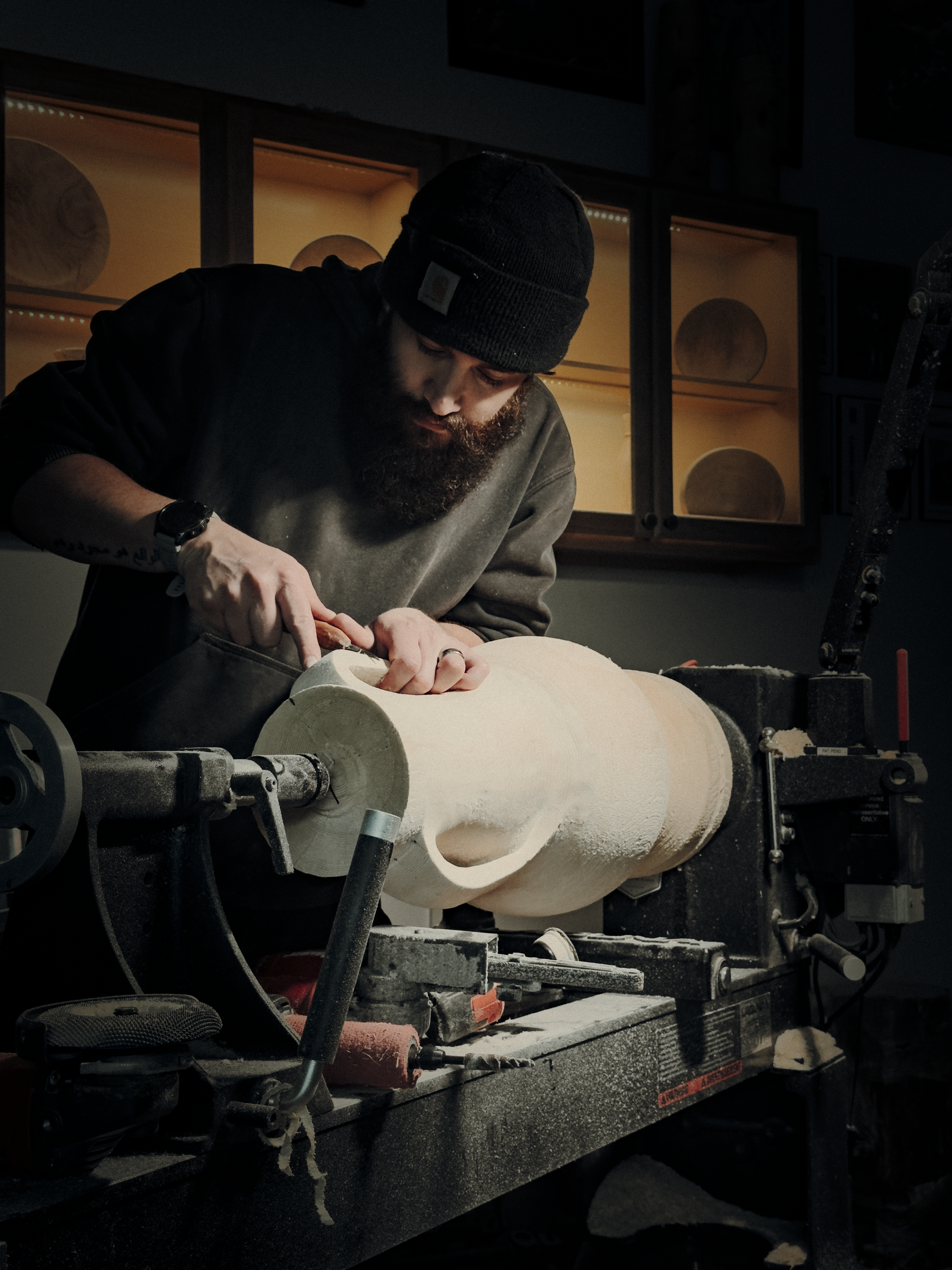 Man working on a wooden sculpture lathe in a workshop.