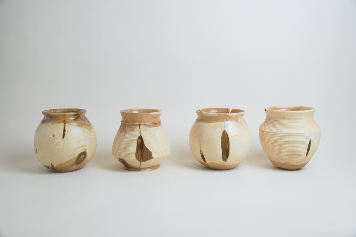 Four pottery vases with natural wood grain and crackle effects, each showing visible cracks and repairs, placed in a row on a white background.