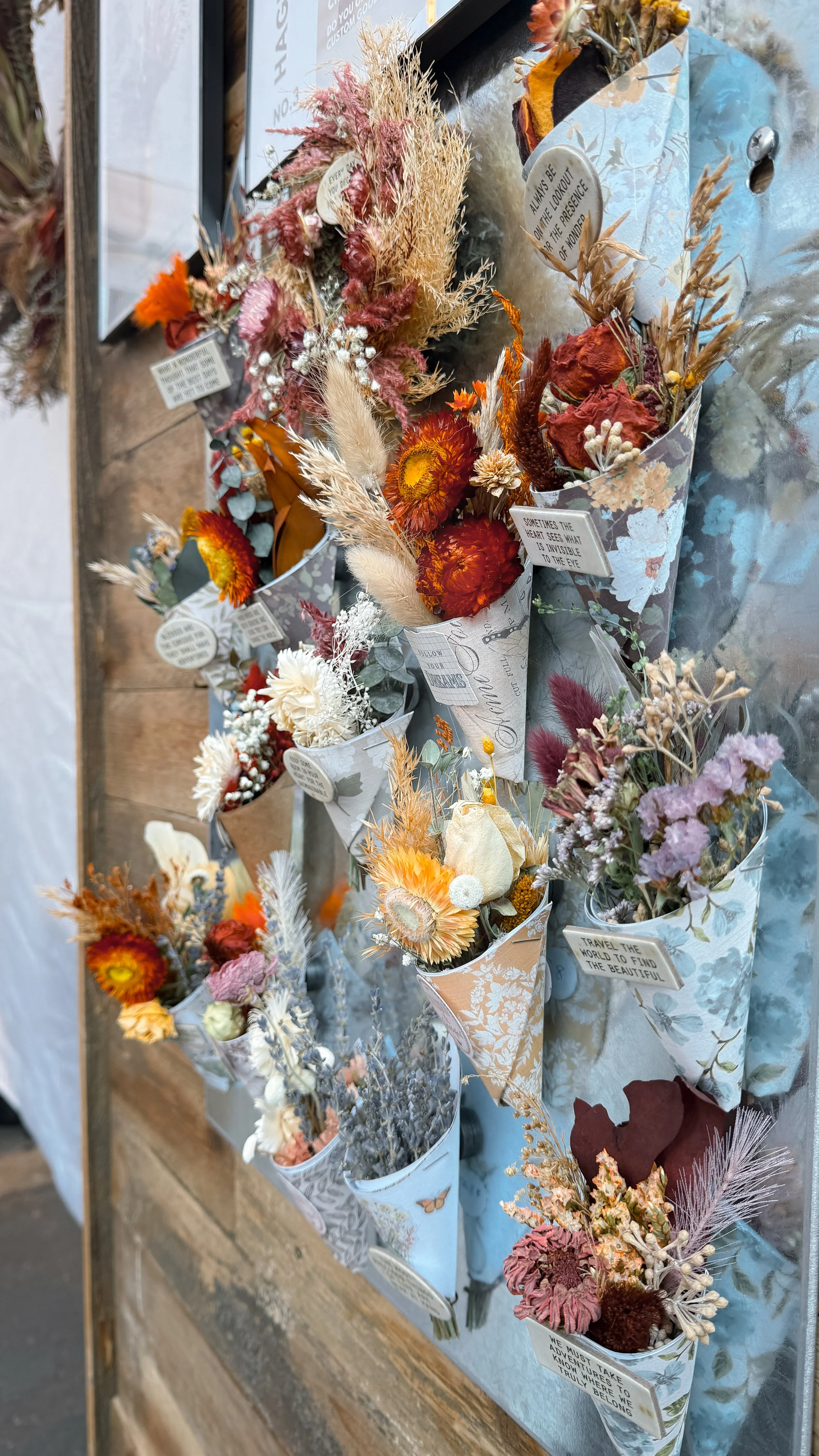 Multiple bouquets of dried and artificial flowers wrapped in decorative paper, displayed on a wooden surface.