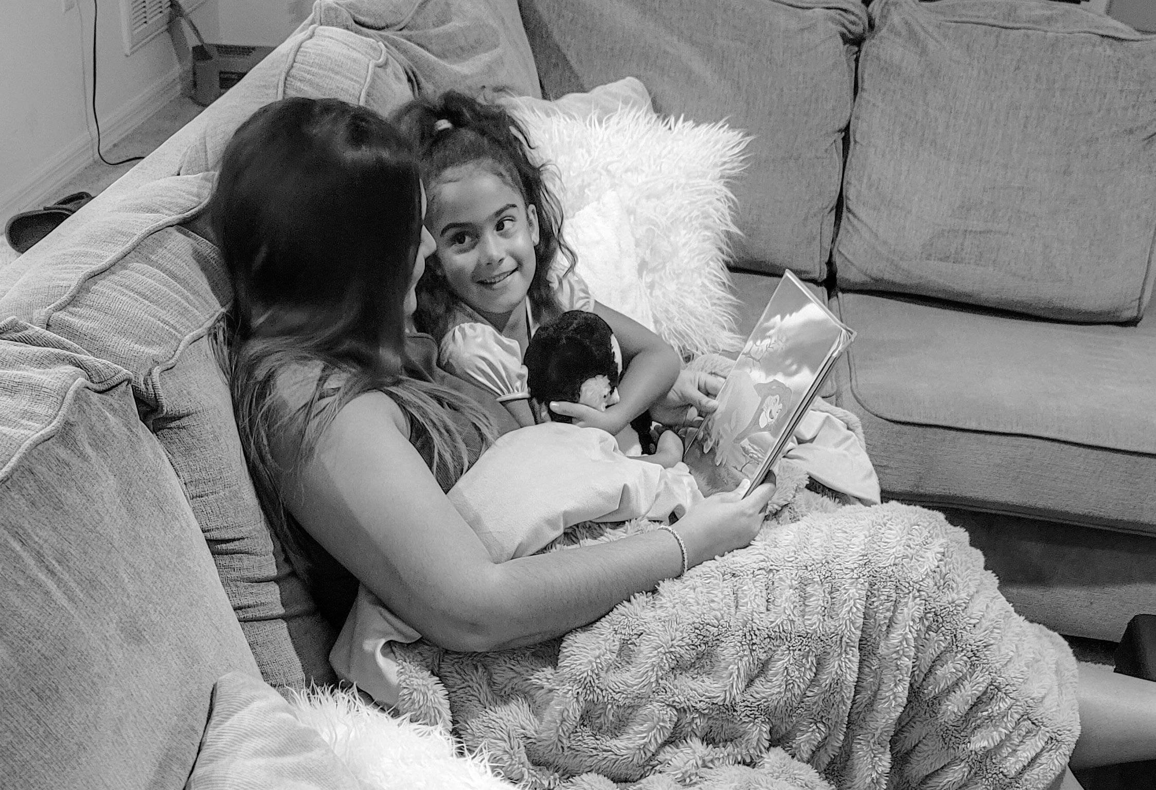 Black and white image of mother and daughter reading while the girl cuddles her teddy.