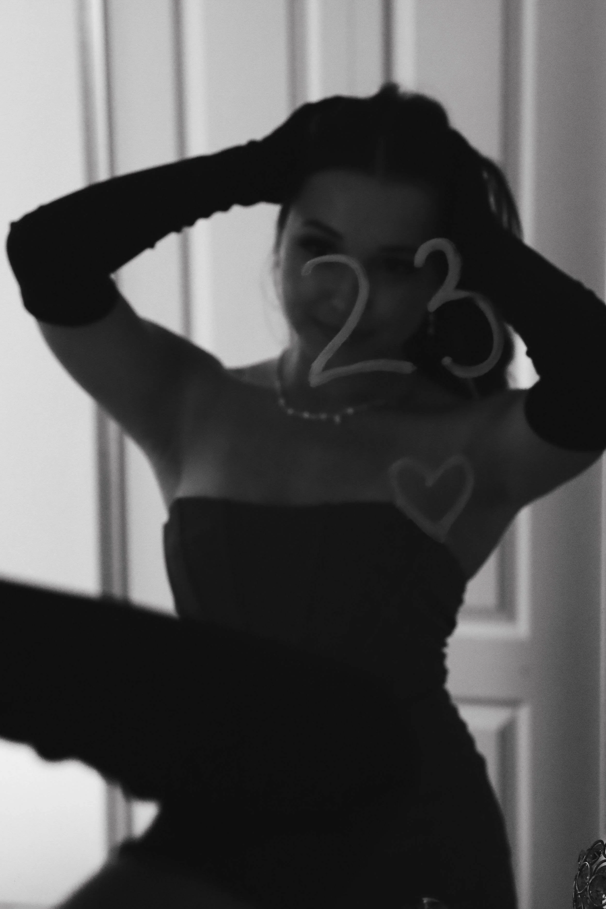 Young woman dressed up fluffing her hair and smiling in the mirror the number 23 written in lipstick on the glass.