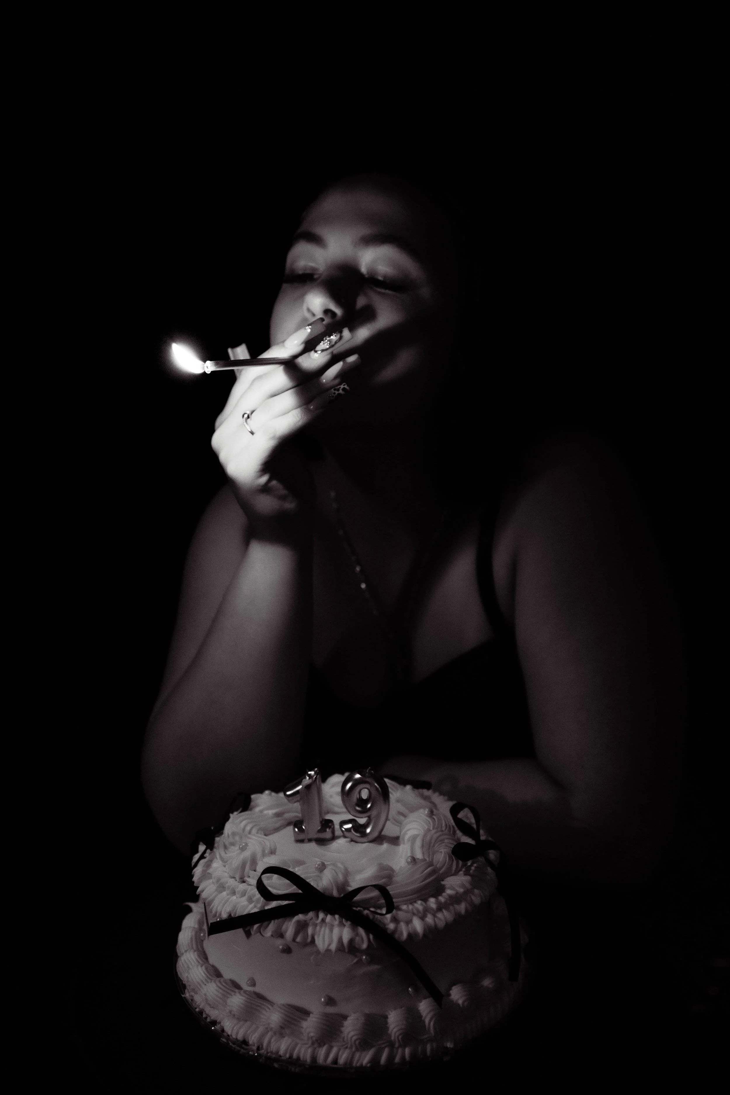 woman with a birthday cake in black and white. The room is dark and she is smoking.