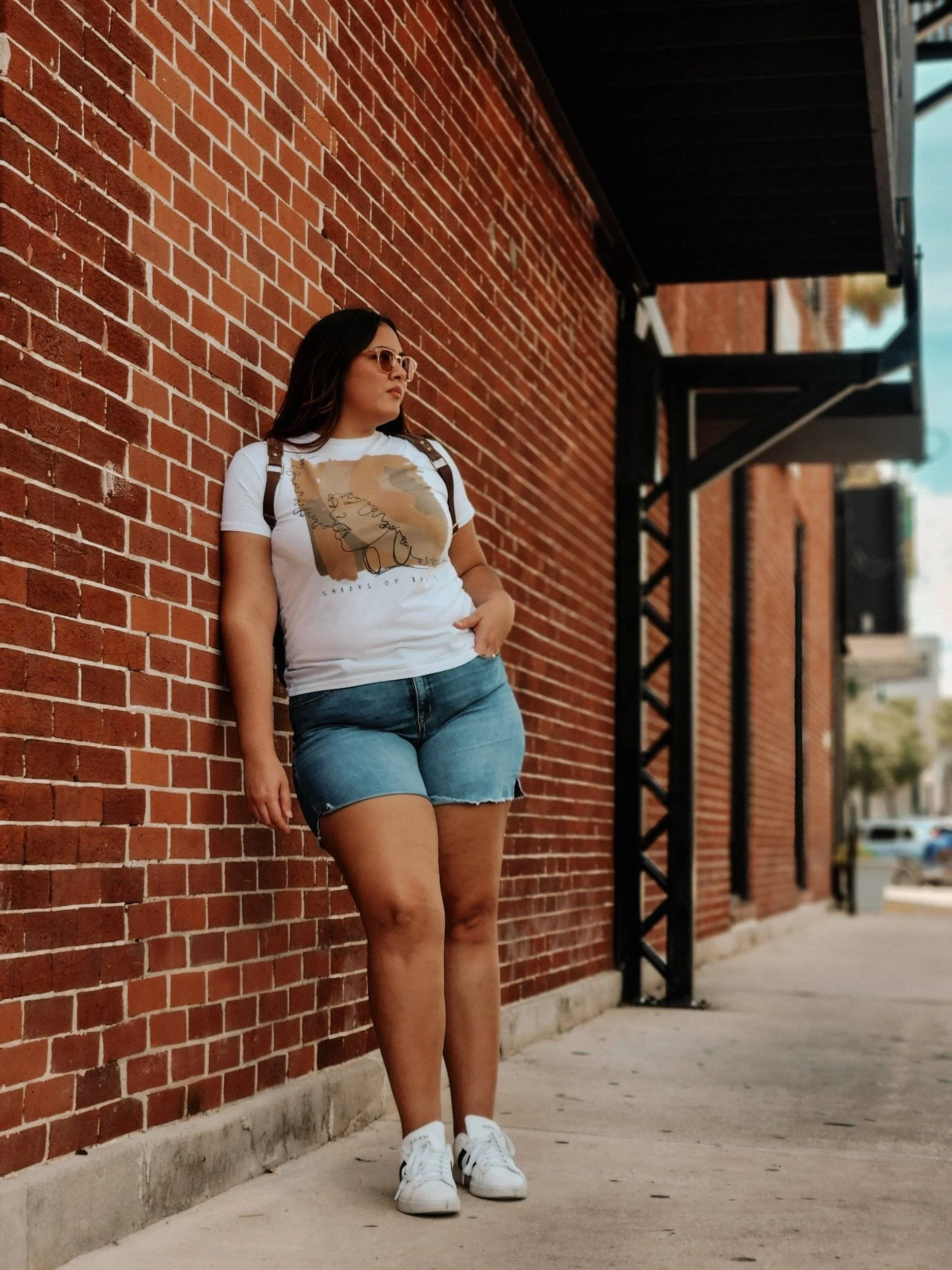 woman in the city leaning on a brick wall and staring at the street.