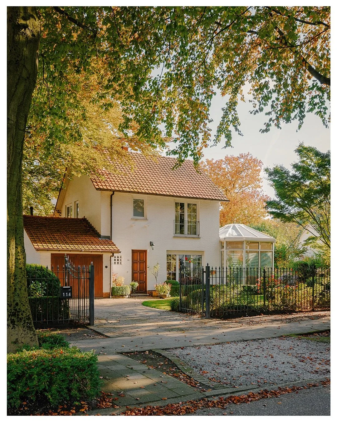 This house glows with autumn&rsquo;s gentle charm,
under the shelter of trees standing tall,
with shadows dancing as daylight wanes,
it whispers of warmth as the evening falls.