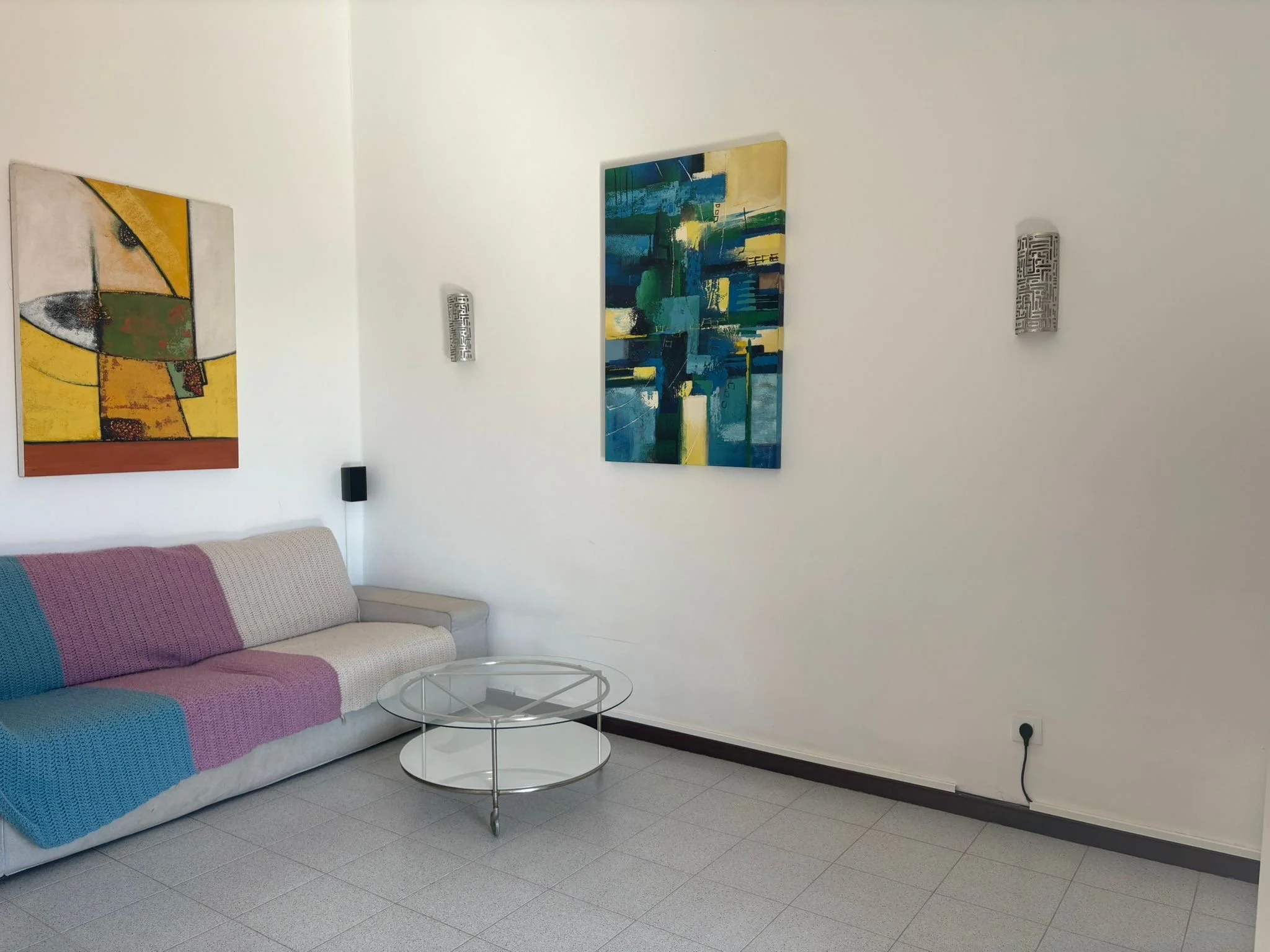 Minimalist living room with abstract paintings, gray sofa, and glass coffee table.