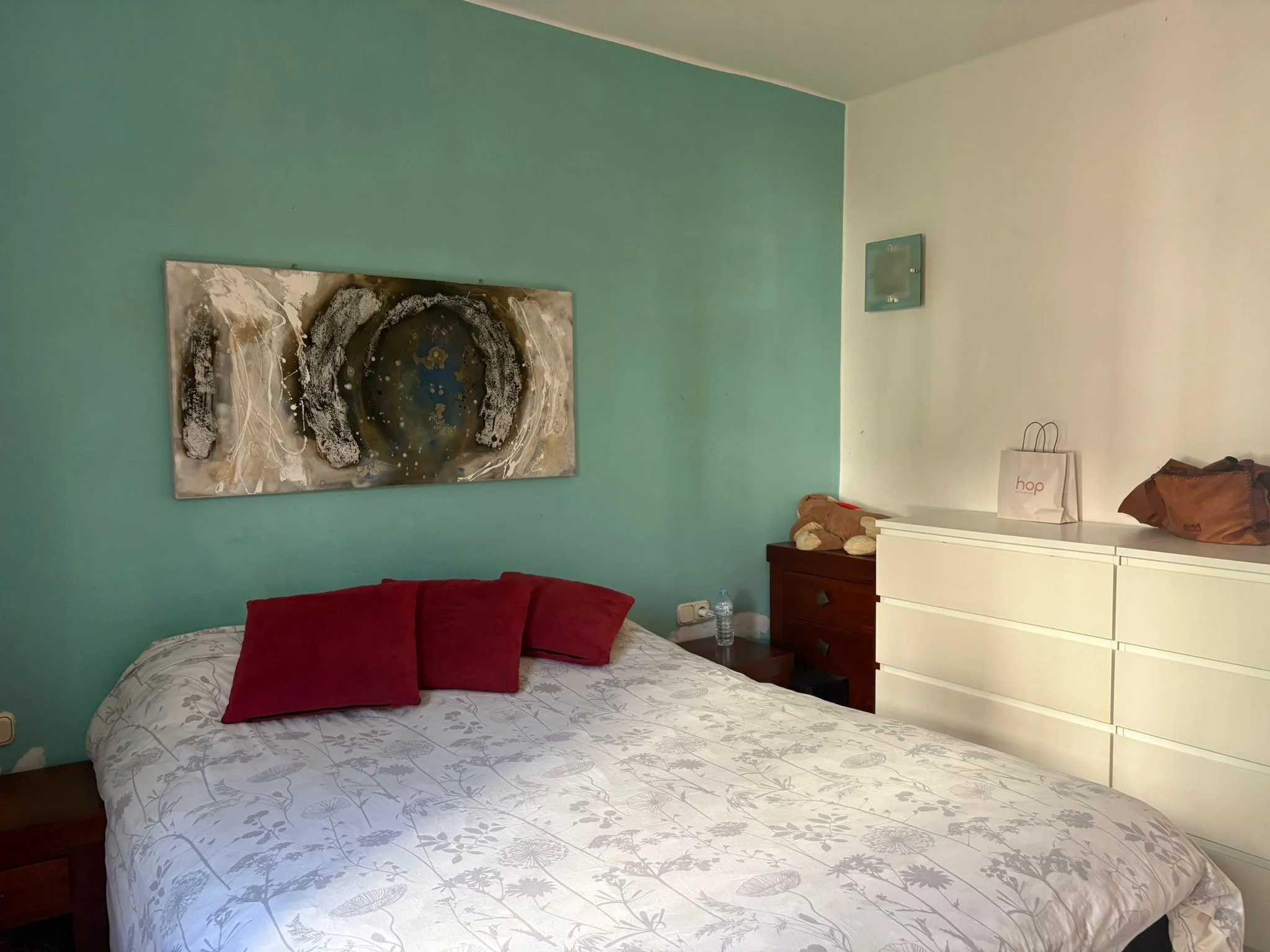 Bedroom interior with bed, red pillows, decorative painting, and white dresser.