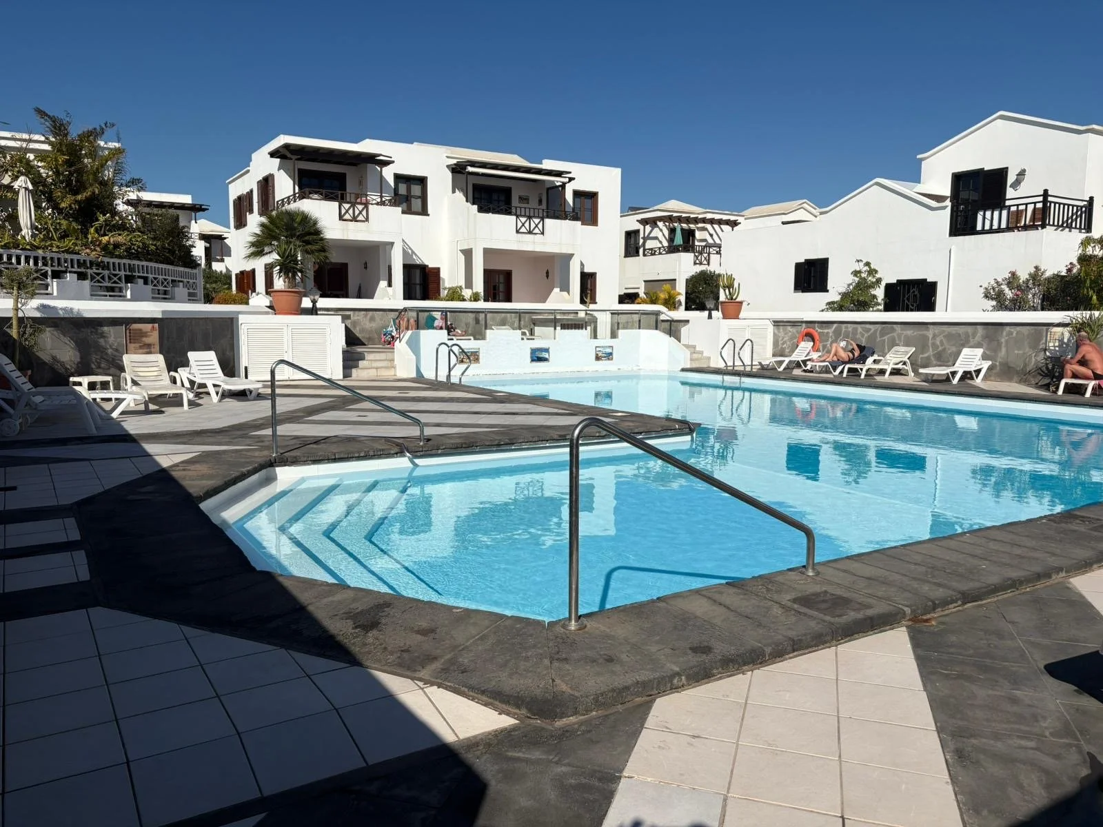 Swimming pool area with white buildings and lounge chairs, clear blue sky