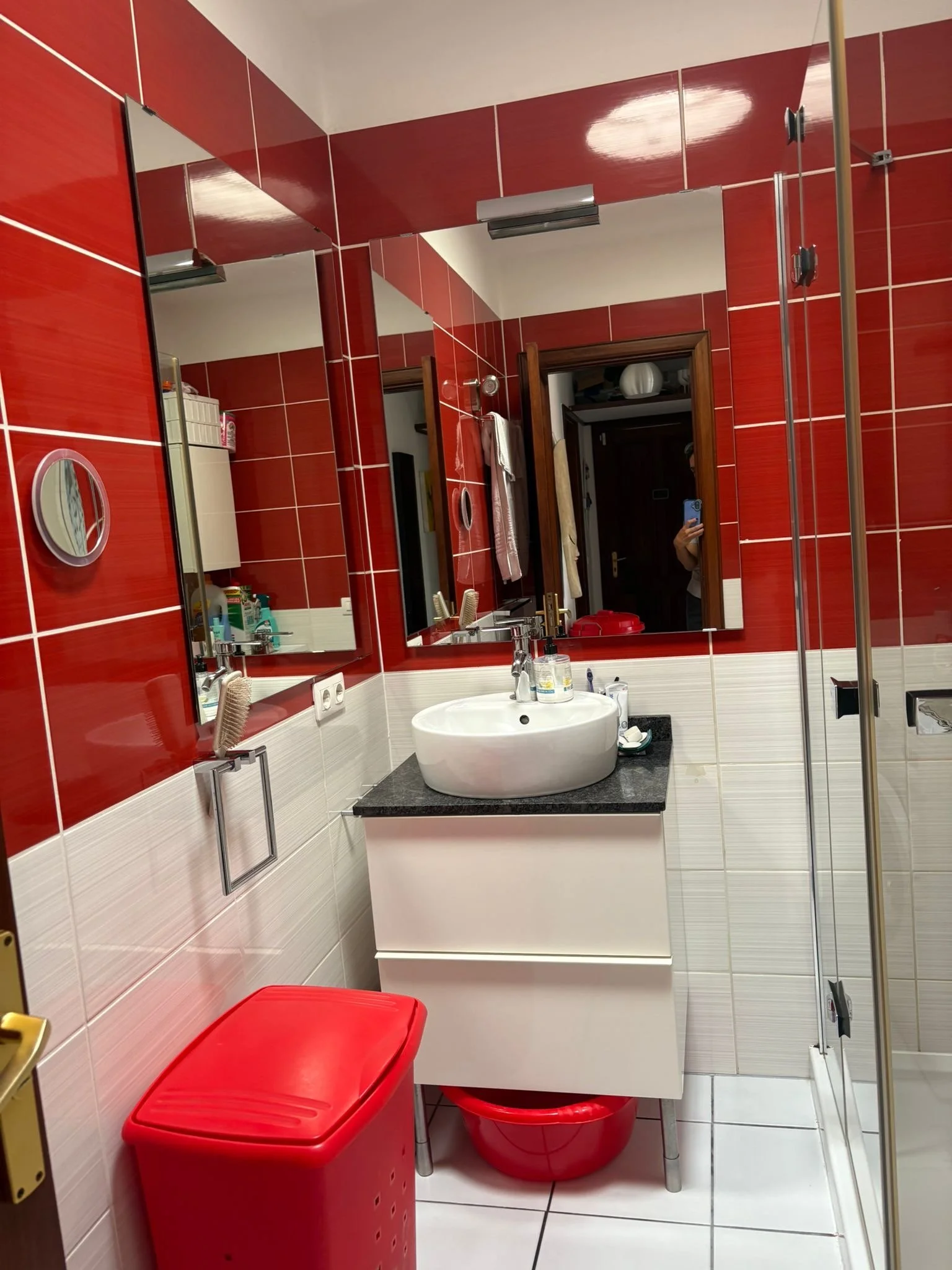 Bathroom with red and white tiles, a sink with a mirror above, a red trash bin, and a shower stall.