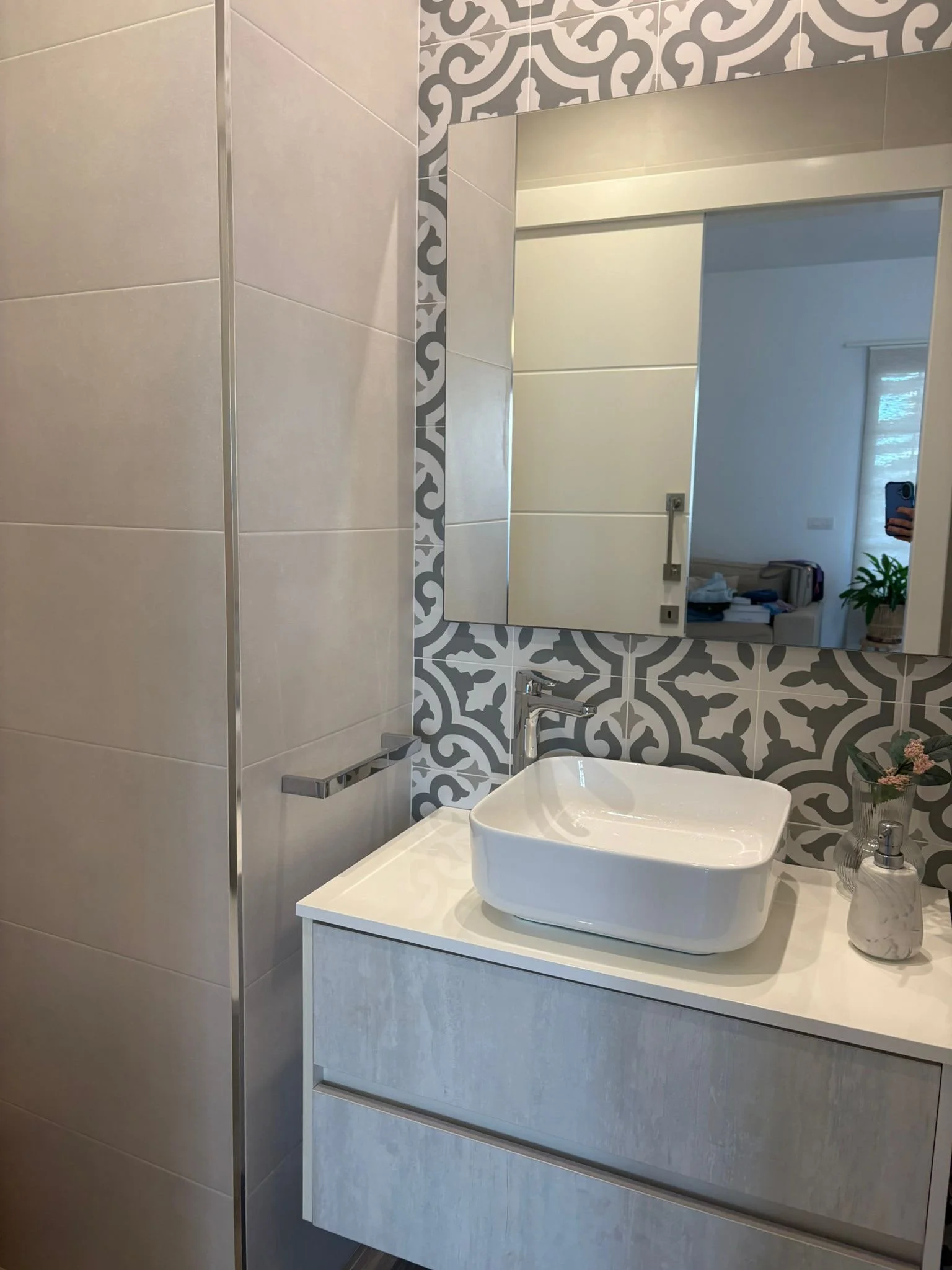 Modern bathroom with rectangular vessel sink on a textured vanity, patterned wall tiles, large mirror, and a soap dispenser.
