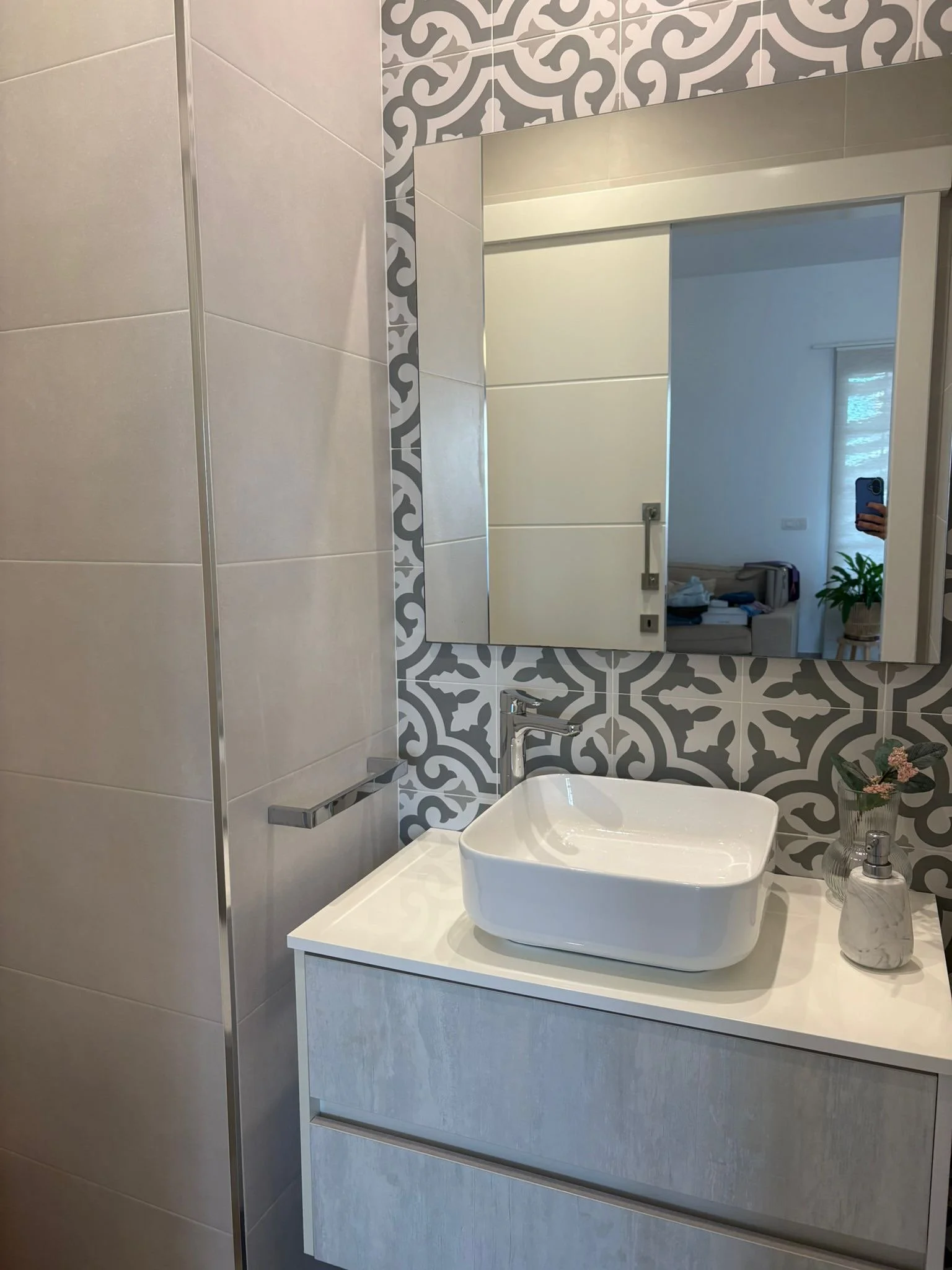 Modern bathroom vanity with white sink, patterned backsplash, mirror, and minimalist decor.