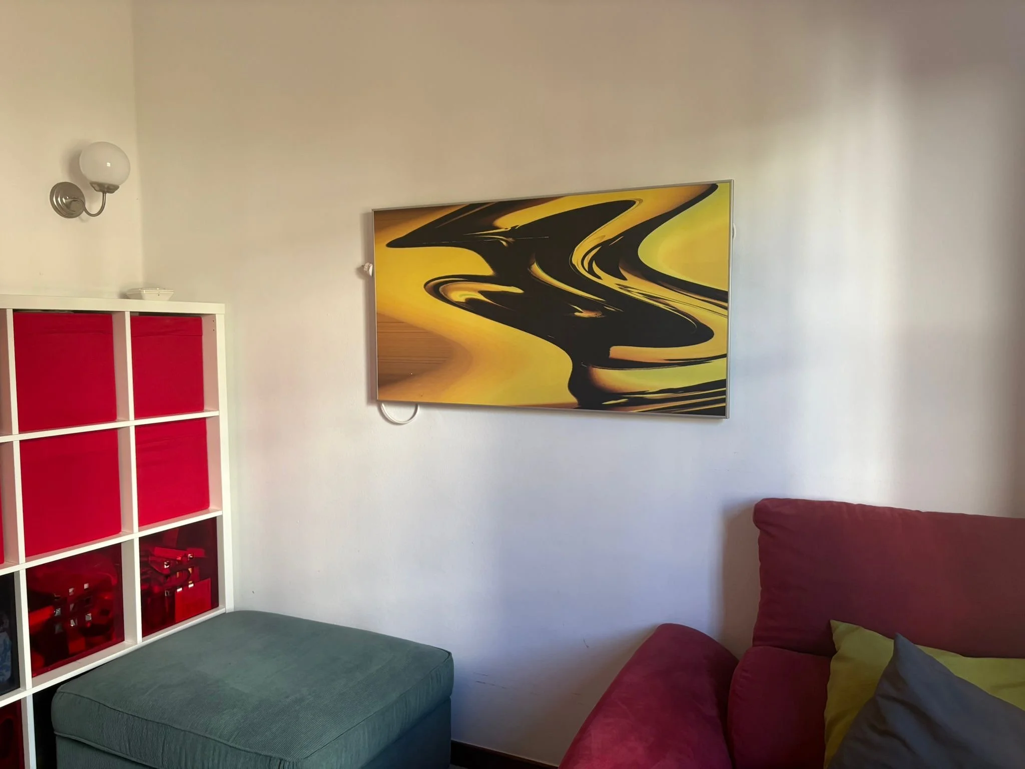 Living room with abstract yellow painting on wall, red armchair, green cushion, blue ottoman, and white cubed shelf with red storage bins.