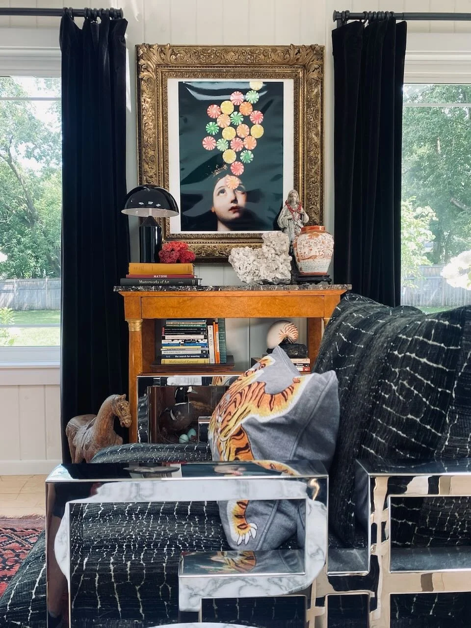 Eclectic living room vignette with black velvet curtains, a vintage wood console, and framed portrait art