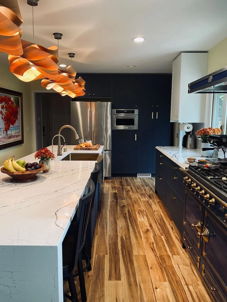 Kitchen with navy cabinets, brass hardware, a white quartz island, and a sculptural orange pendant light