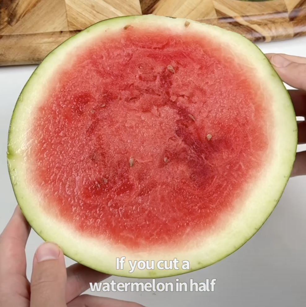 Watermelon sliced in half, showing the red flesh, resting on a wood cutting board.