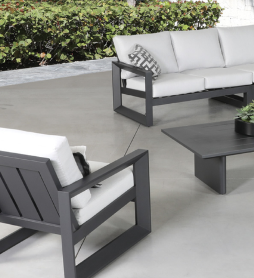 Charcoal-framed Rose Casual sofa and lounge chair with white cushions and a patterned throw pillow, paired with a matching coffee table on a concrete patio, greenery behind.