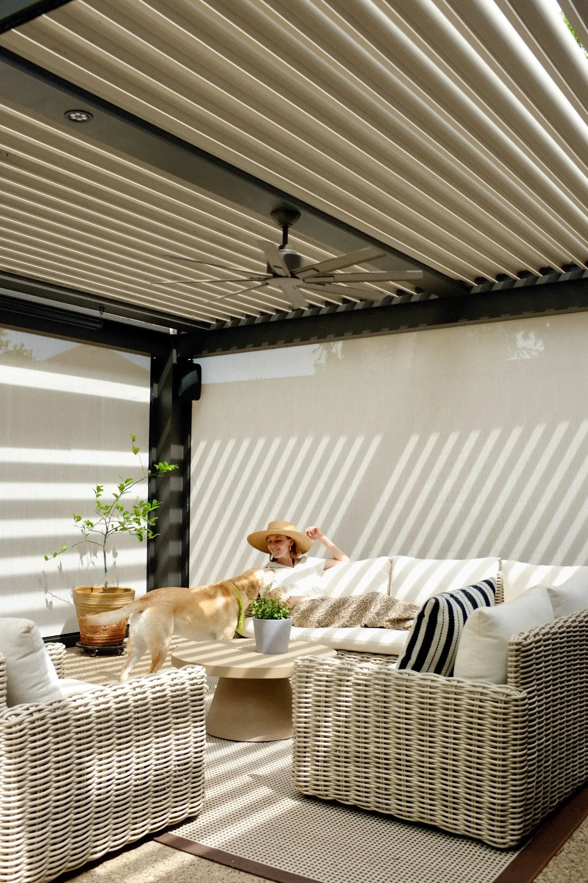 A woman lounging on a patio set and looking at her dog under a StruXure pergolas by Goodlux Outdoor