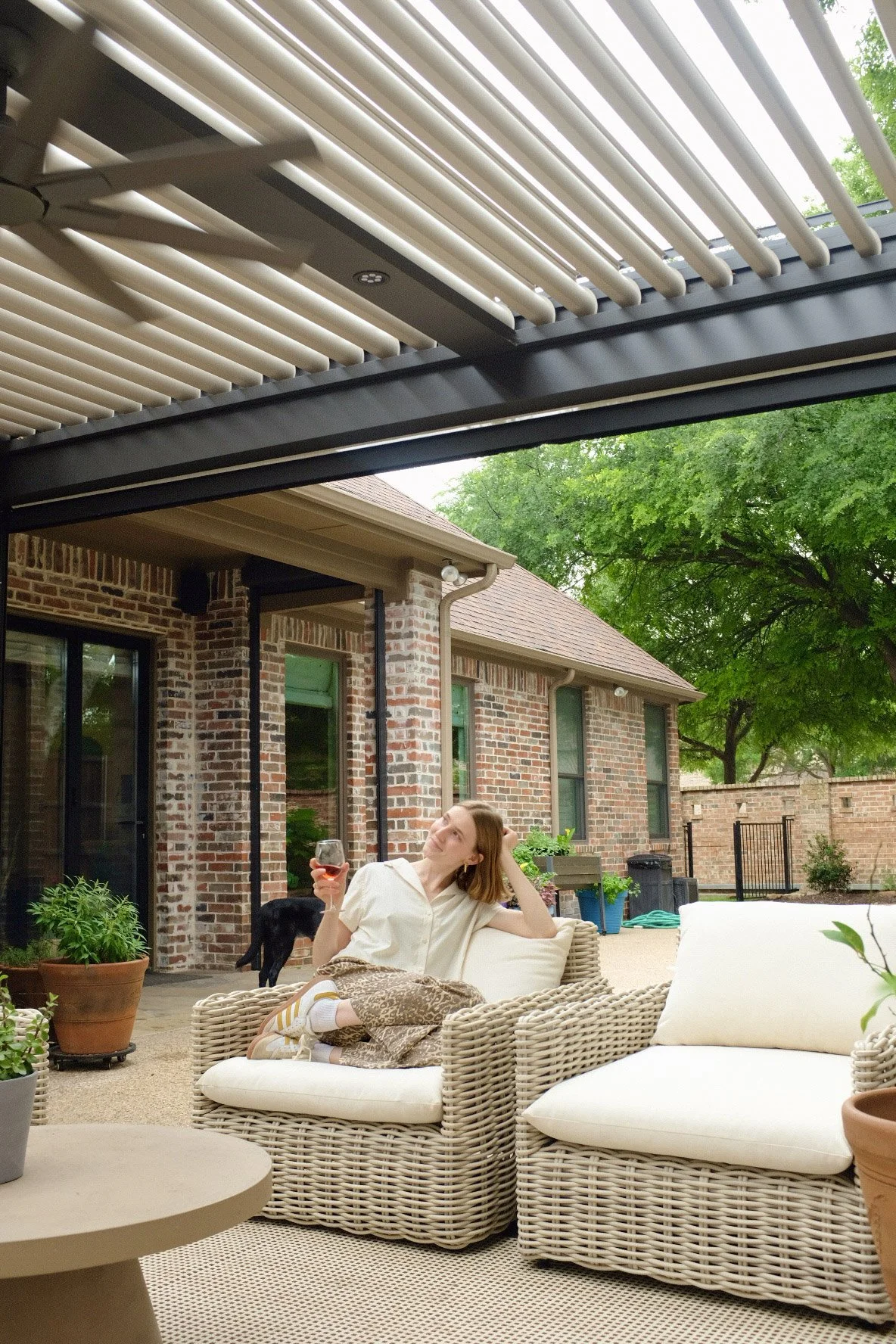 A woman sitting on patio furniture looking up at her StruXure Pergola by Goodlux Outdoor drinking a glass of win